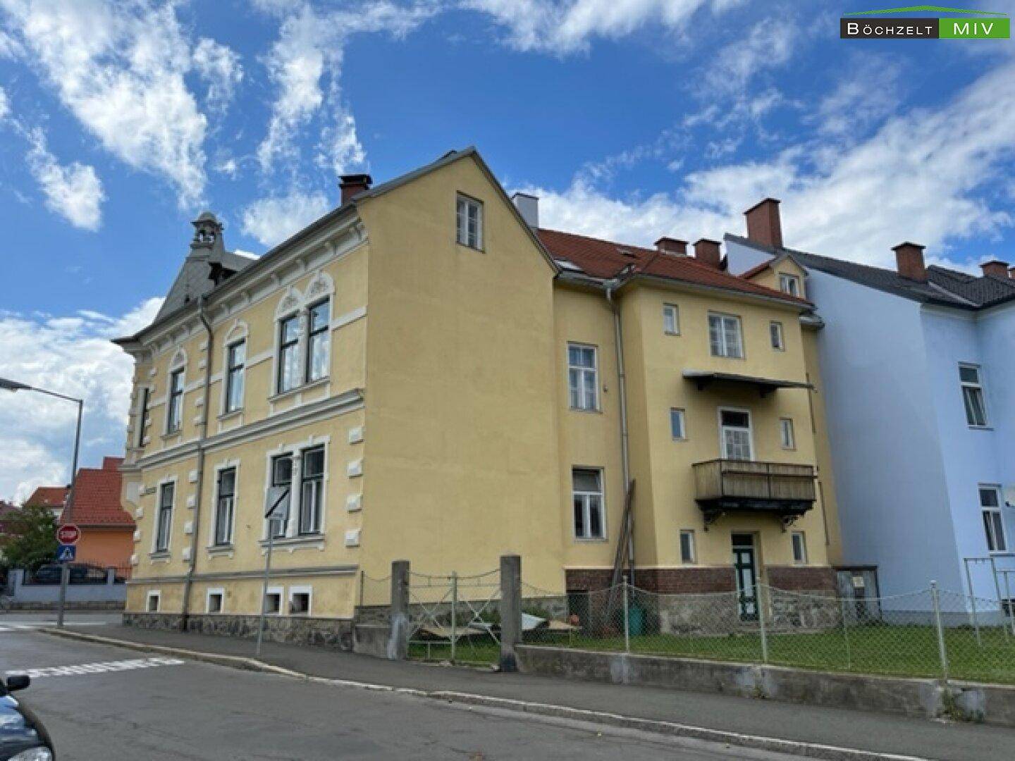 Seitenansicht des historischen Gebäudes mit Balkon und angrenzenden Wohnhäusern.