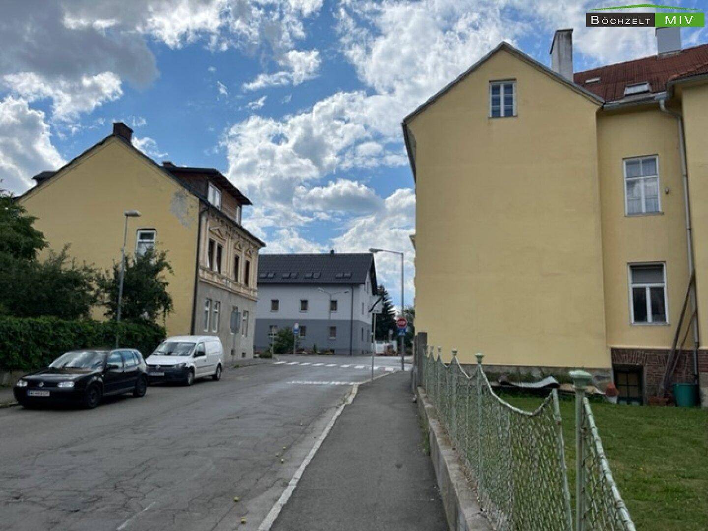 Blick auf die Straße mit parkenden Autos und weiteren Wohnhäusern in der Umgebung.