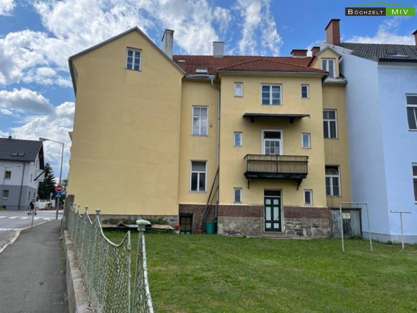 Rückansicht des historischen Gebäudes mit Balkon und Blick auf die umliegende Grünfläche.