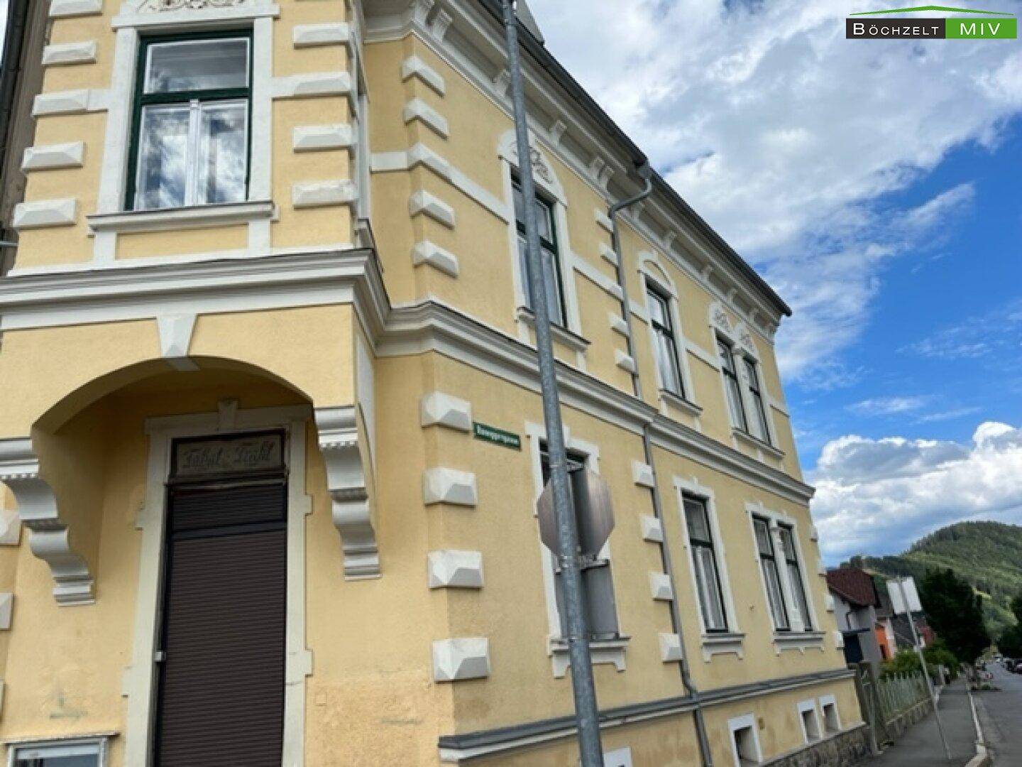 Detailansicht der gelben Fassade des historischen Gebäudes mit dekorativen Fensterrahmen.