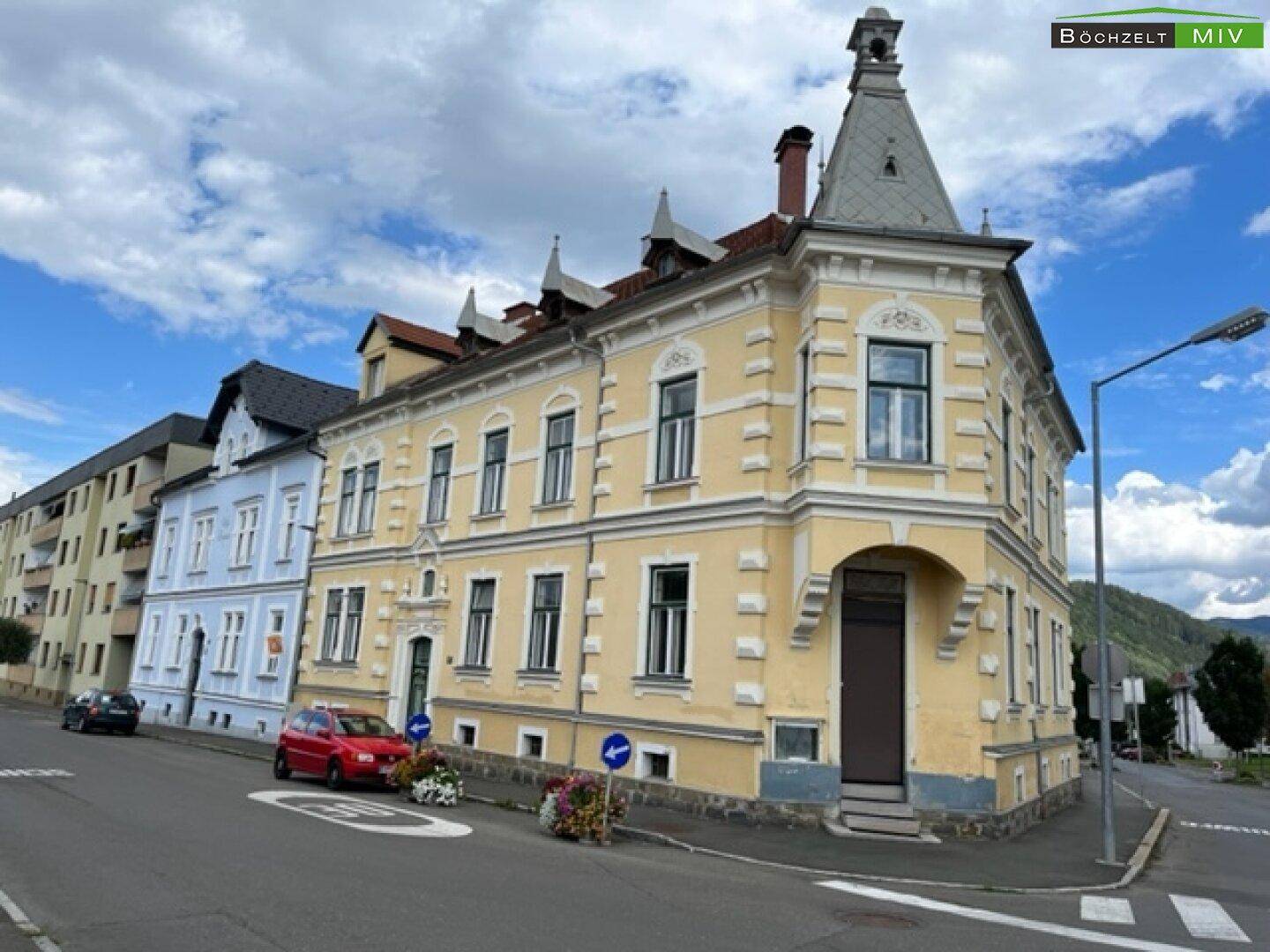 Detailansicht des historischen Eckgebäudes mit gelber Fassade und dekorativen Elementen.
