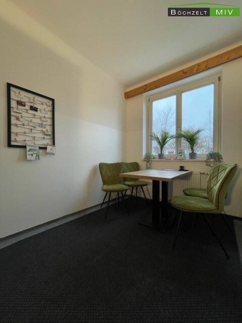 Gemütlicher Sitzbereich in einem hellen Raum mit Teppichboden und einem Fenster mit Blick nach draußen.