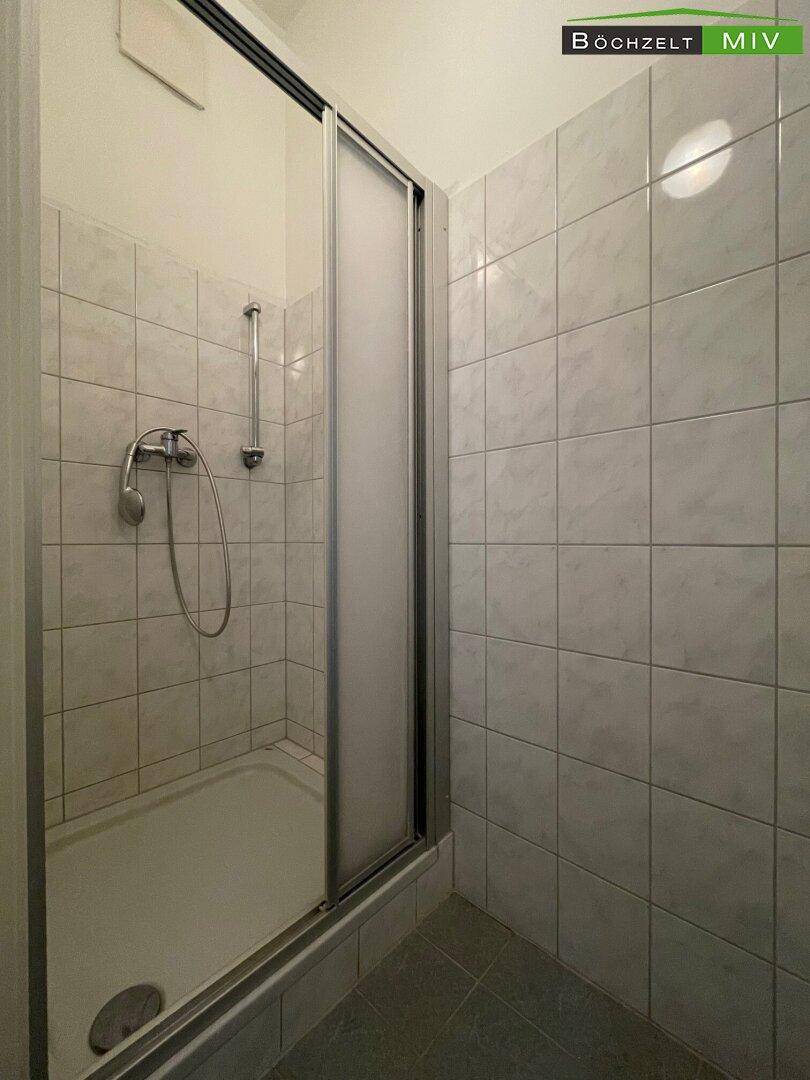Gefliestes Badezimmer mit einer Duschkabine und einfacher Armatur.