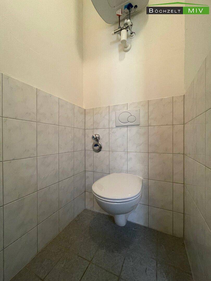 Kleiner Toilettenraum mit wandhängendem WC und hellen Fliesen an den Wänden.