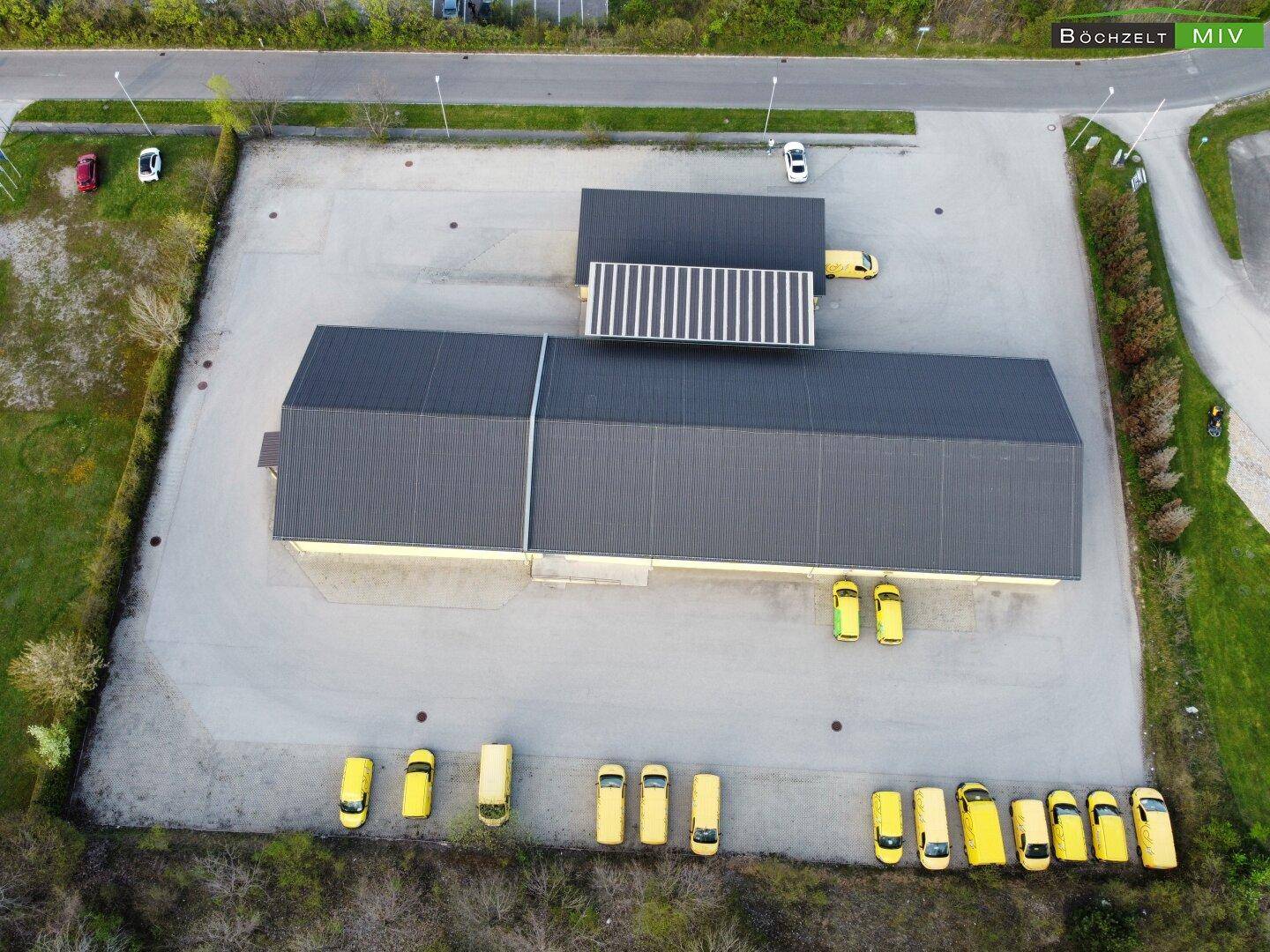 Senkrechte Luftaufnahme des Gewerbegebäudes mit dunklem Dach und zahlreichen gelben Lieferwagen.
