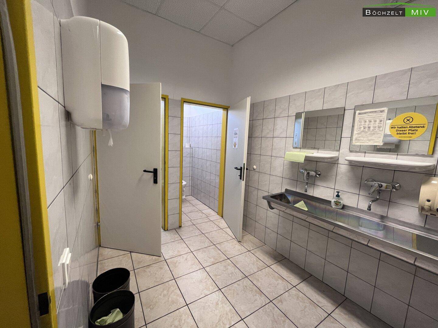 Waschbereich im Sanitärraum mit Fliesen, mehreren Waschbecken und Spiegeln.