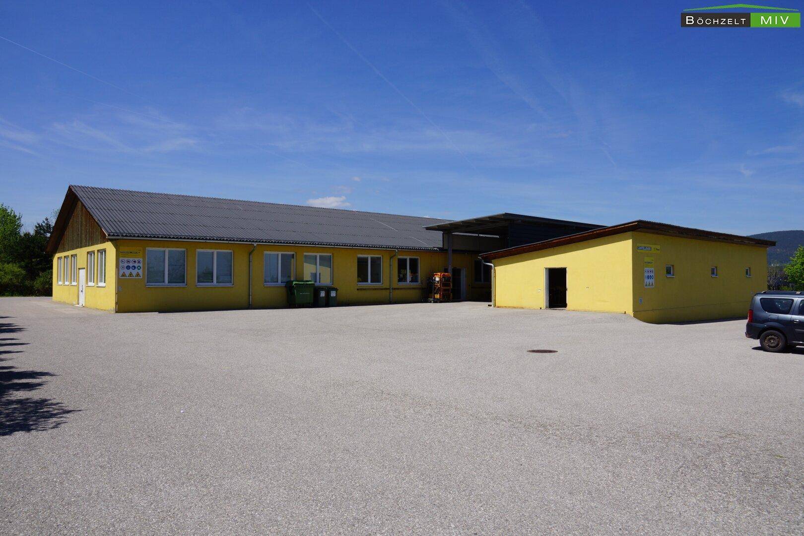 Ansicht des gelben Gewerbegebäudes mit großem, gepflastertem Vorplatz unter blauem Himmel.