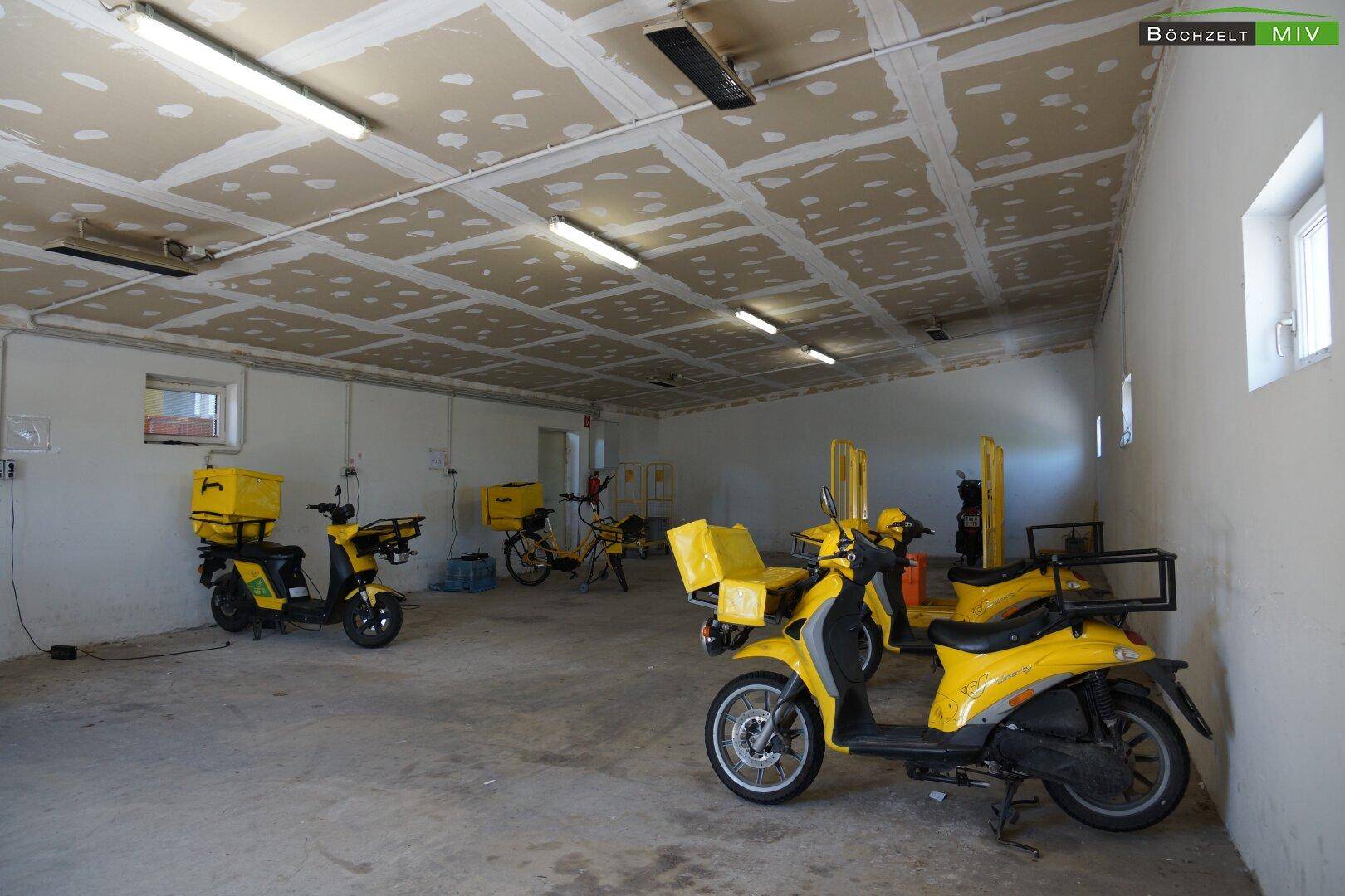 Großer Raum mit mehreren gelben Rollern und Fahrrädern, vermutlich eine Fahrzeuggarage.