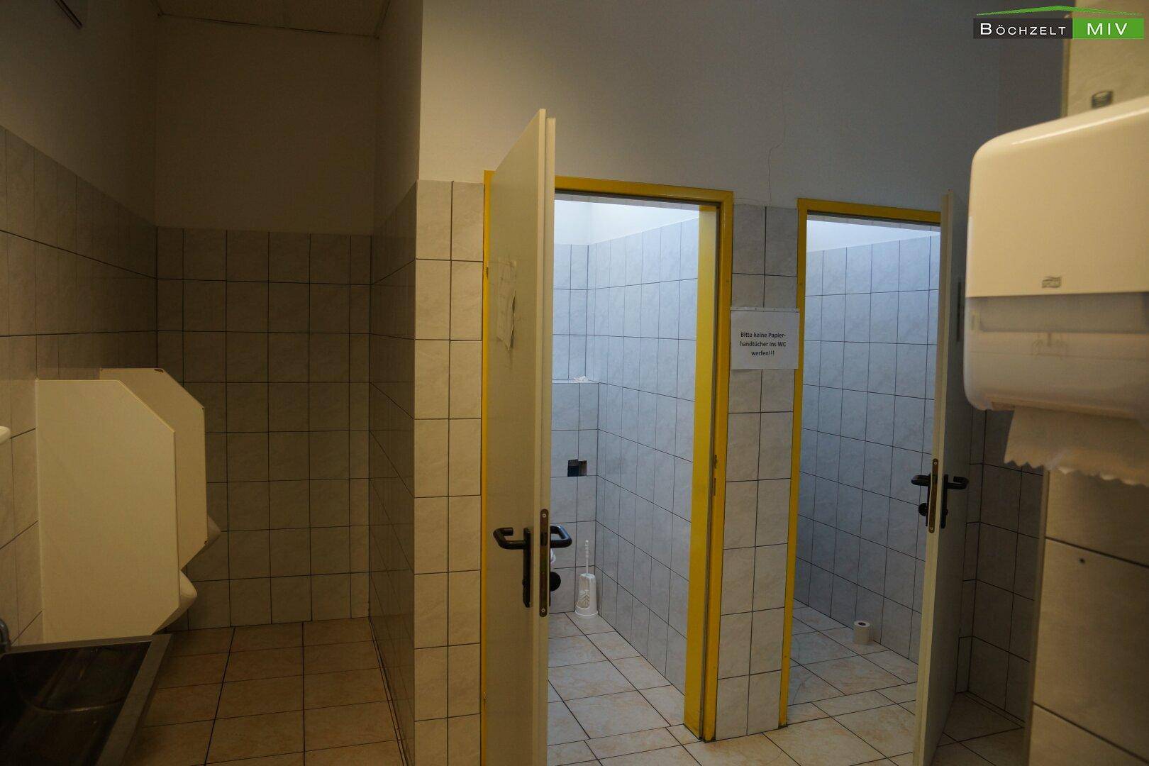 Sanitärbereich mit gefliesten Wänden, mehreren Toilettenkabinen und einem Waschbecken.