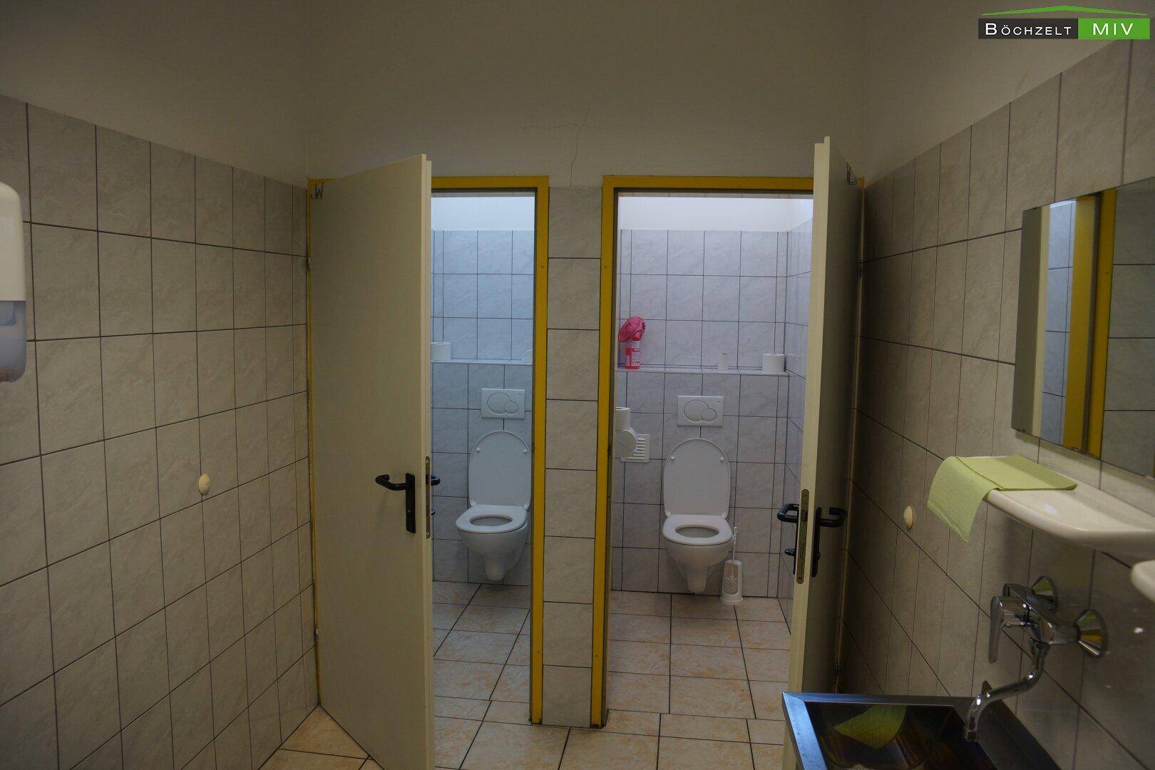 Zwei Toilettenkabinen in einem gefliesten Sanitärraum, sauber und funktional.