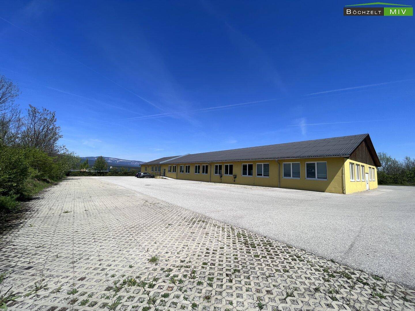 Weitläufiger gepflasterter Bereich neben dem gelben Gewerbegebäude mit Blick auf die Landschaft.