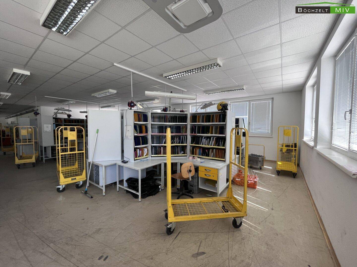 Arbeitsplatz in einem offenen Büro mit Sortierregalen und ergonomischem Stuhl, gut beleuchtet und funktional.