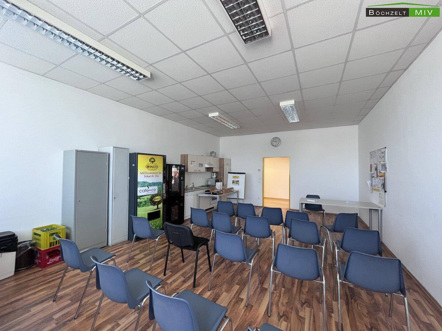 Konferenzraum mit Stühlen, Tischen und einer kleinen Küchenzeile, ideal für Besprechungen und Pausen.