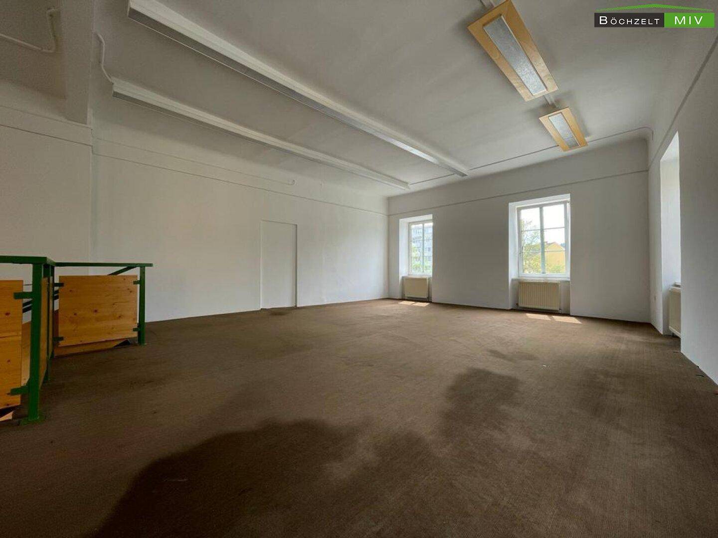 Heller Obergeschossraum mit Teppichboden und mehreren Fenstern, die viel Tageslicht hereinlassen.