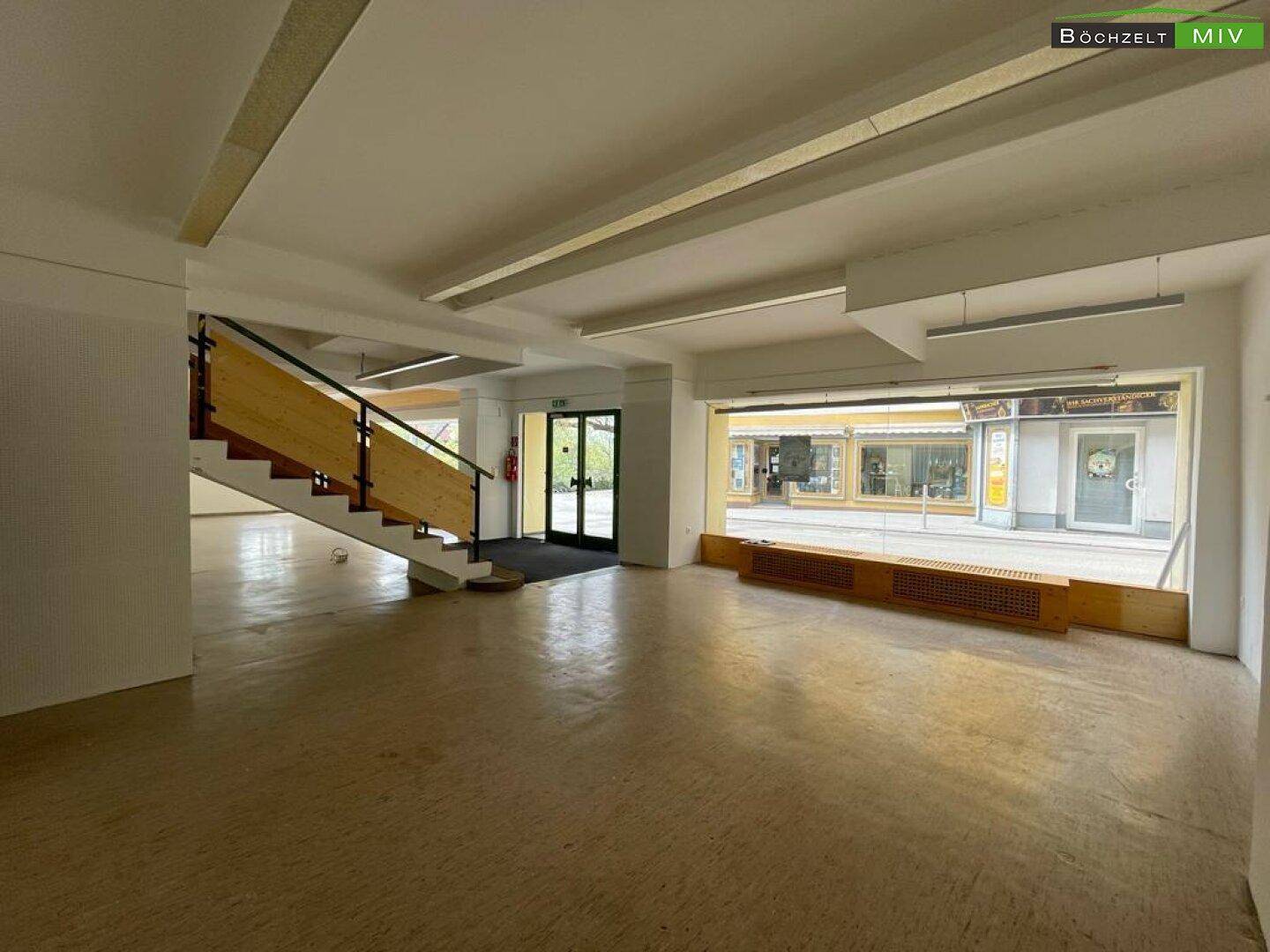 Offener Verkaufsraum mit viel Tageslicht, einer Treppe und Blick auf die Straße durch die Schaufenster.