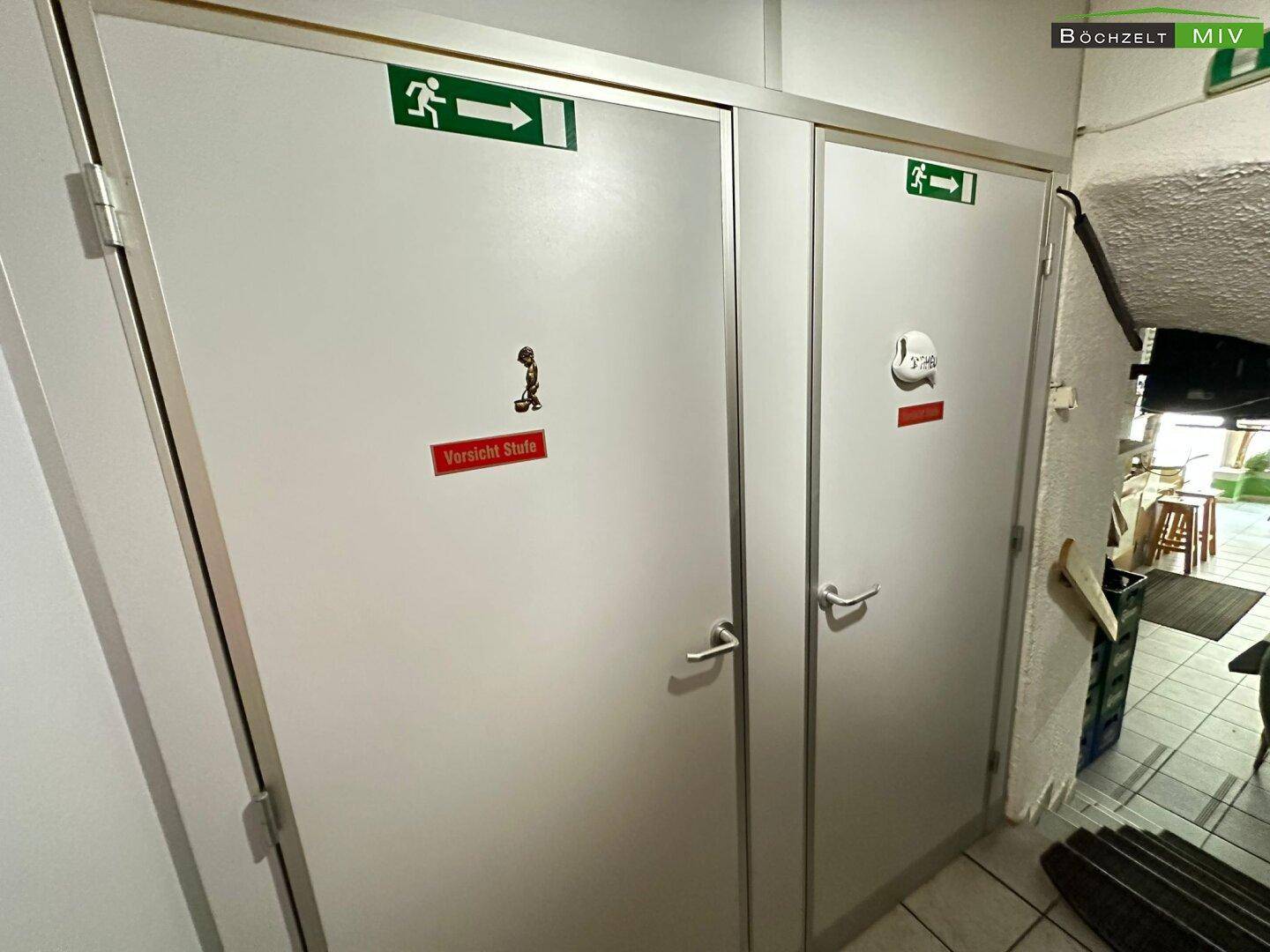 Zwei Türen zu Toilettenräumen mit Notausgangsschildern und Hinweisen.