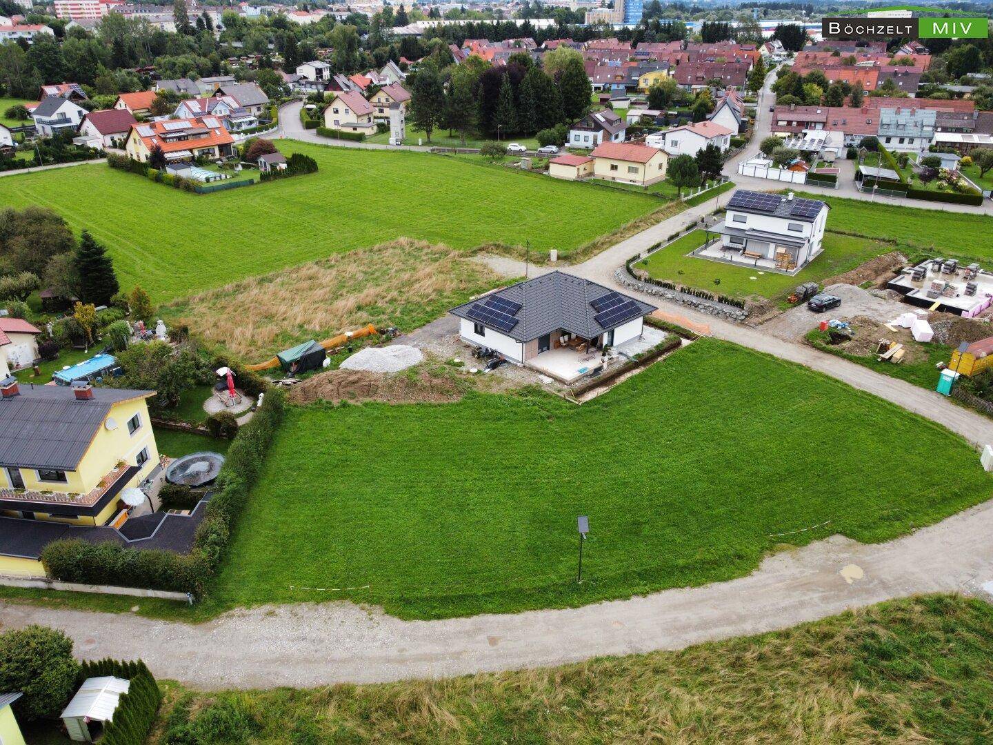 Panoramablick auf ein neues Wohnhaus mit Solarpaneelen, eingebettet in eine grüne Landschaft mit Bergsicht.