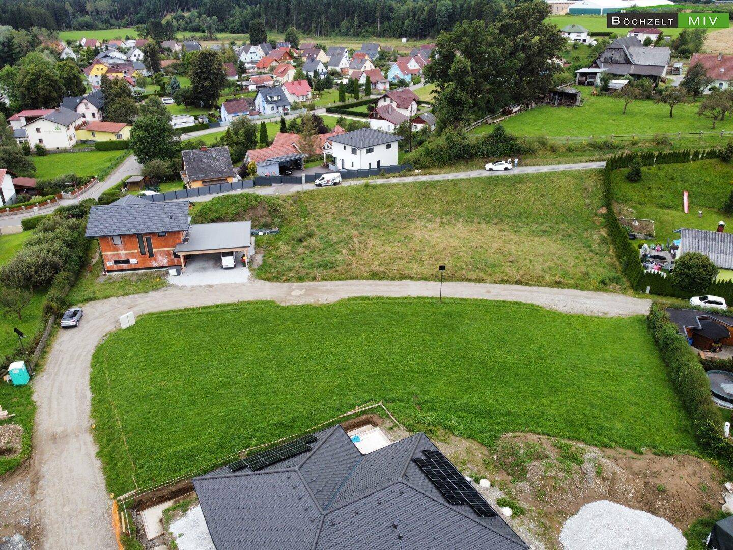 Luftaufnahme eines Neubauprojekts mit bereits errichtetem Dach und umliegenden Wohnhäusern in ländlicher Lage.