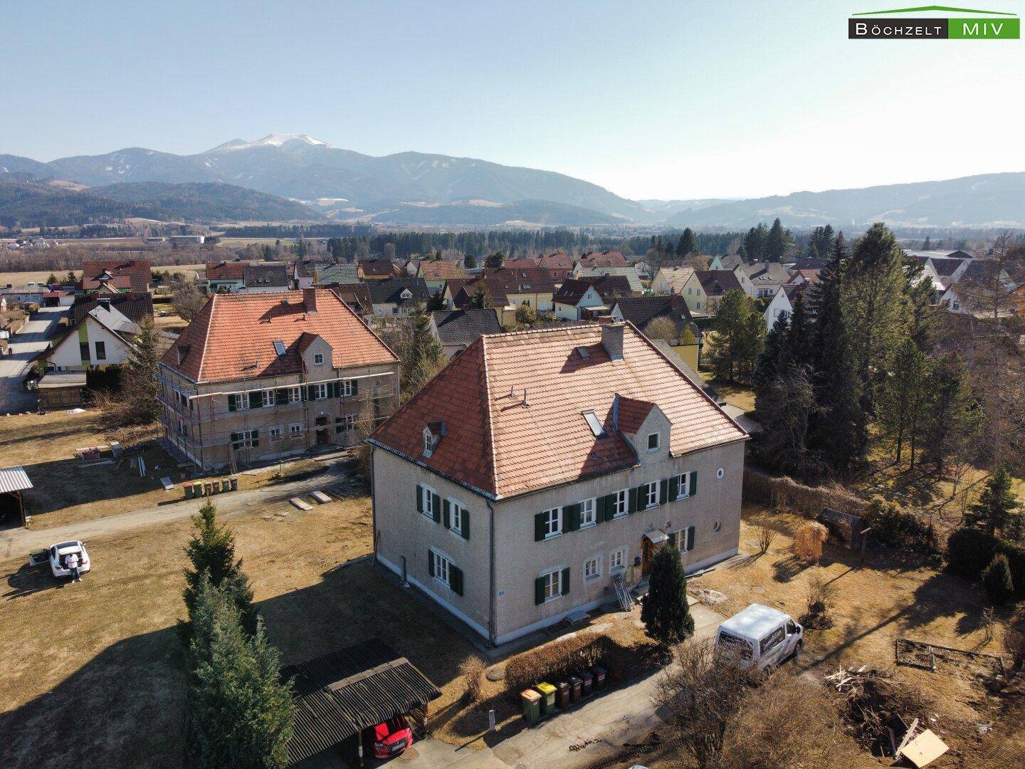 Luftaufnahme von zwei Gebäuden mit roten Ziegeldächern in ländlicher Umgebung mit Bergblick.