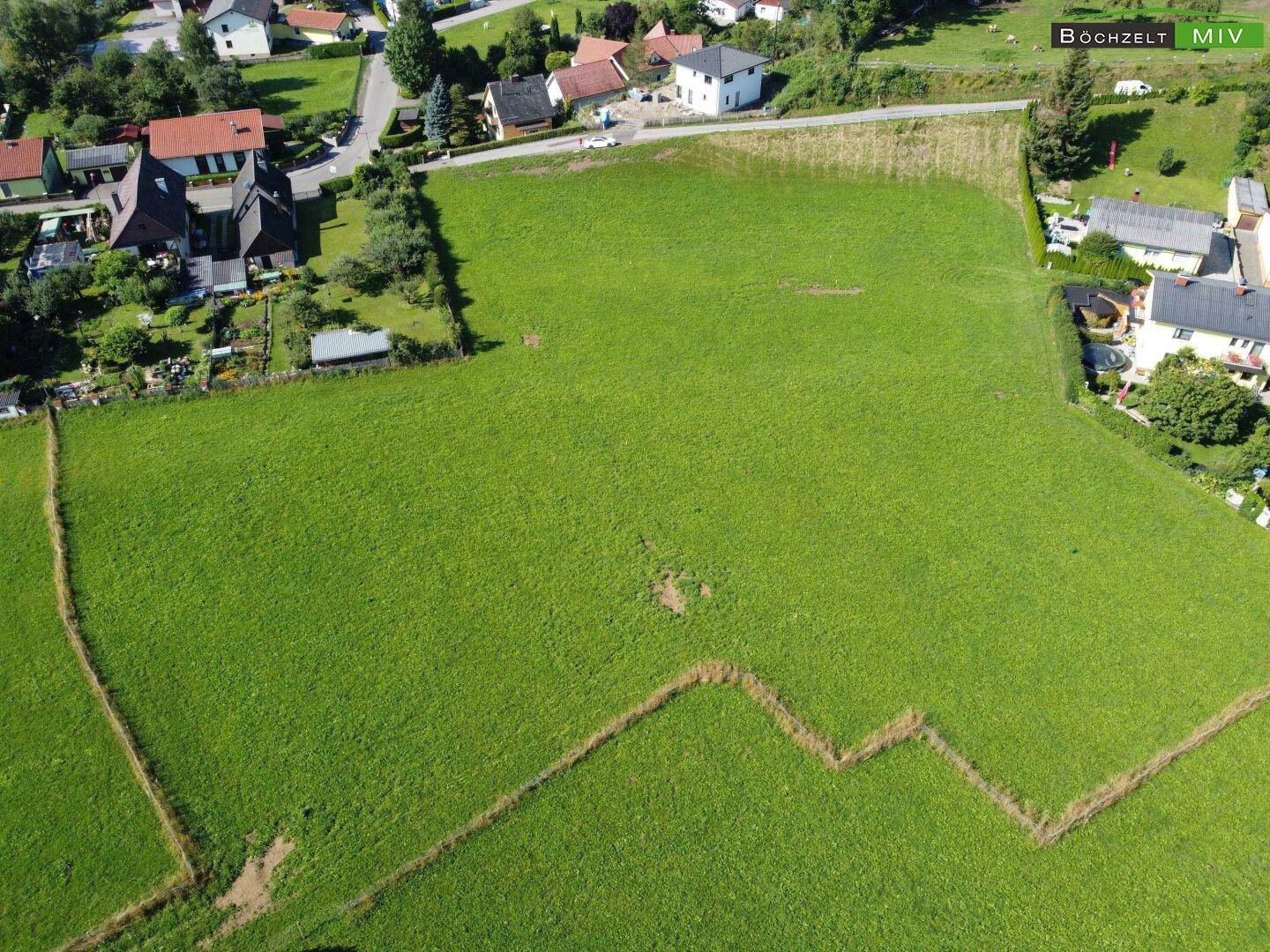 Luftaufnahme eines weitläufigen grünen Grundstücks, umgeben von Wohnbebauung und Natur.