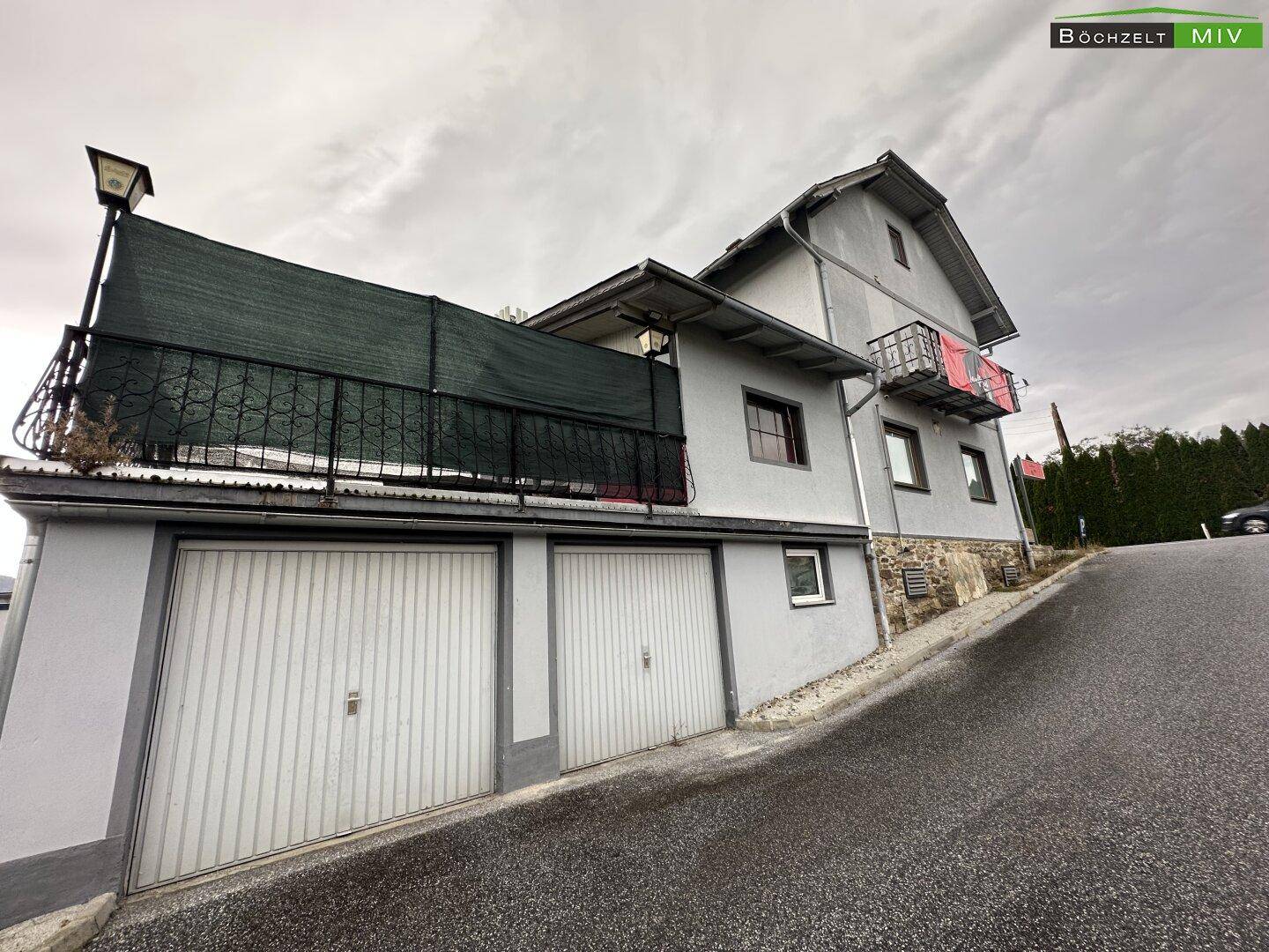 Seitenansicht des Gebäudes mit zwei Garagentoren im Erdgeschoss und einem kleinen Balkon im oberen Stockwerk.