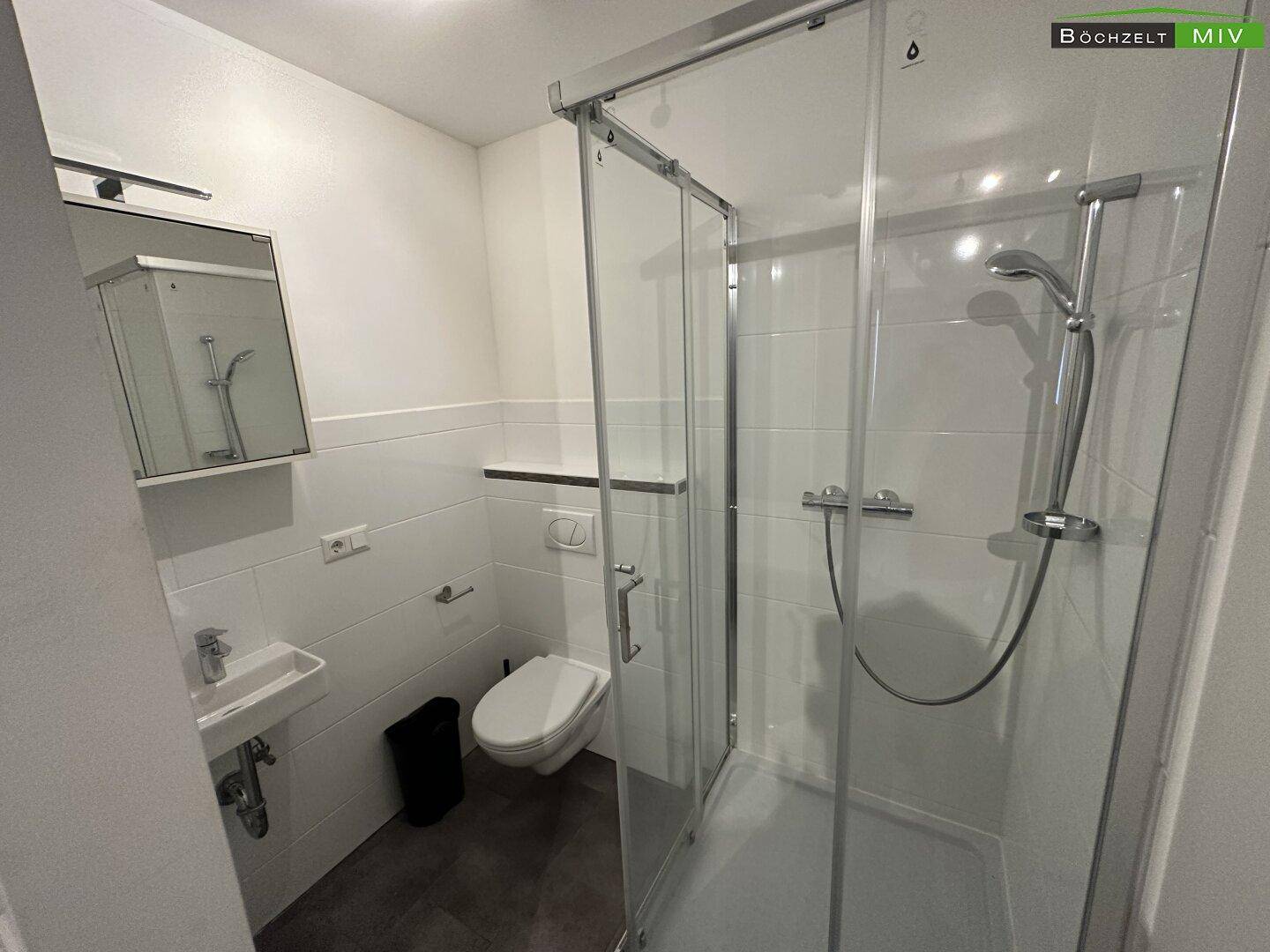 Modernes Badezimmer mit Duschkabine, Waschbecken und wandhängendem WC, alles in hellen Farben gehalten.