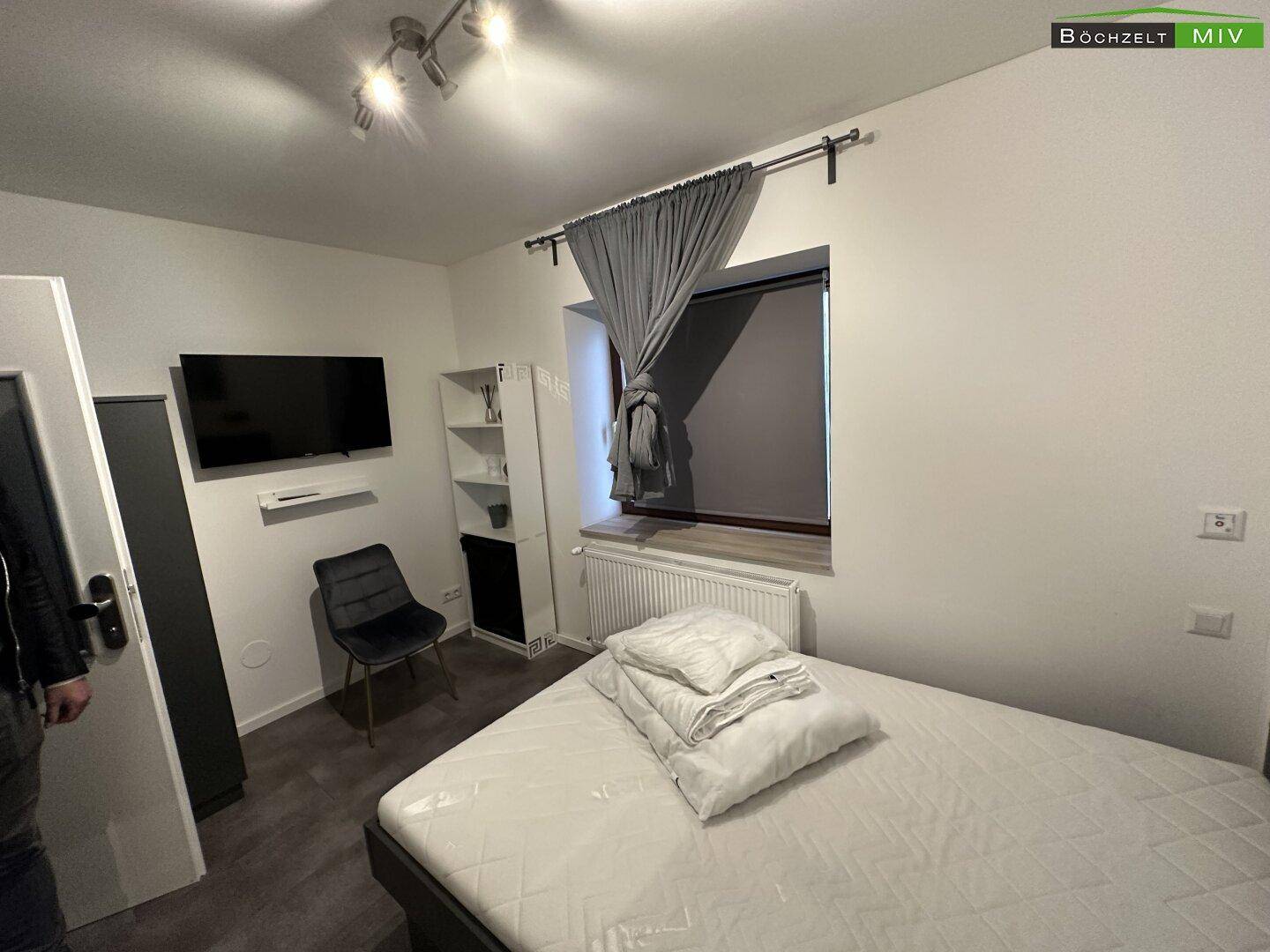 Schlafzimmer mit Bett, Fenster und Heizkörper, ausgestattet mit dunklen Vorhängen und modernem Dekor.