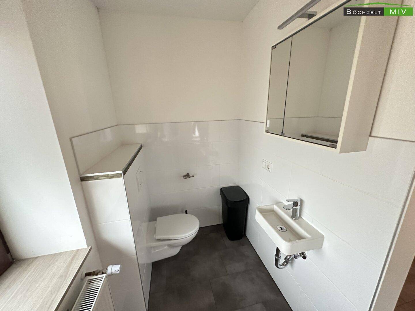 Helles Badezimmer mit wandhängendem WC, kleinem Waschbecken und Spiegelschrank, modern gefliest.