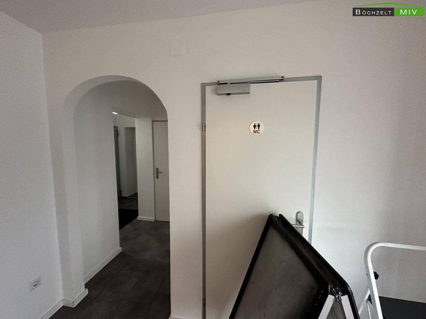 Flur mit einem eleganten Bogen und einer Tür, die zu den Toiletten führt, in schlichtem Design.