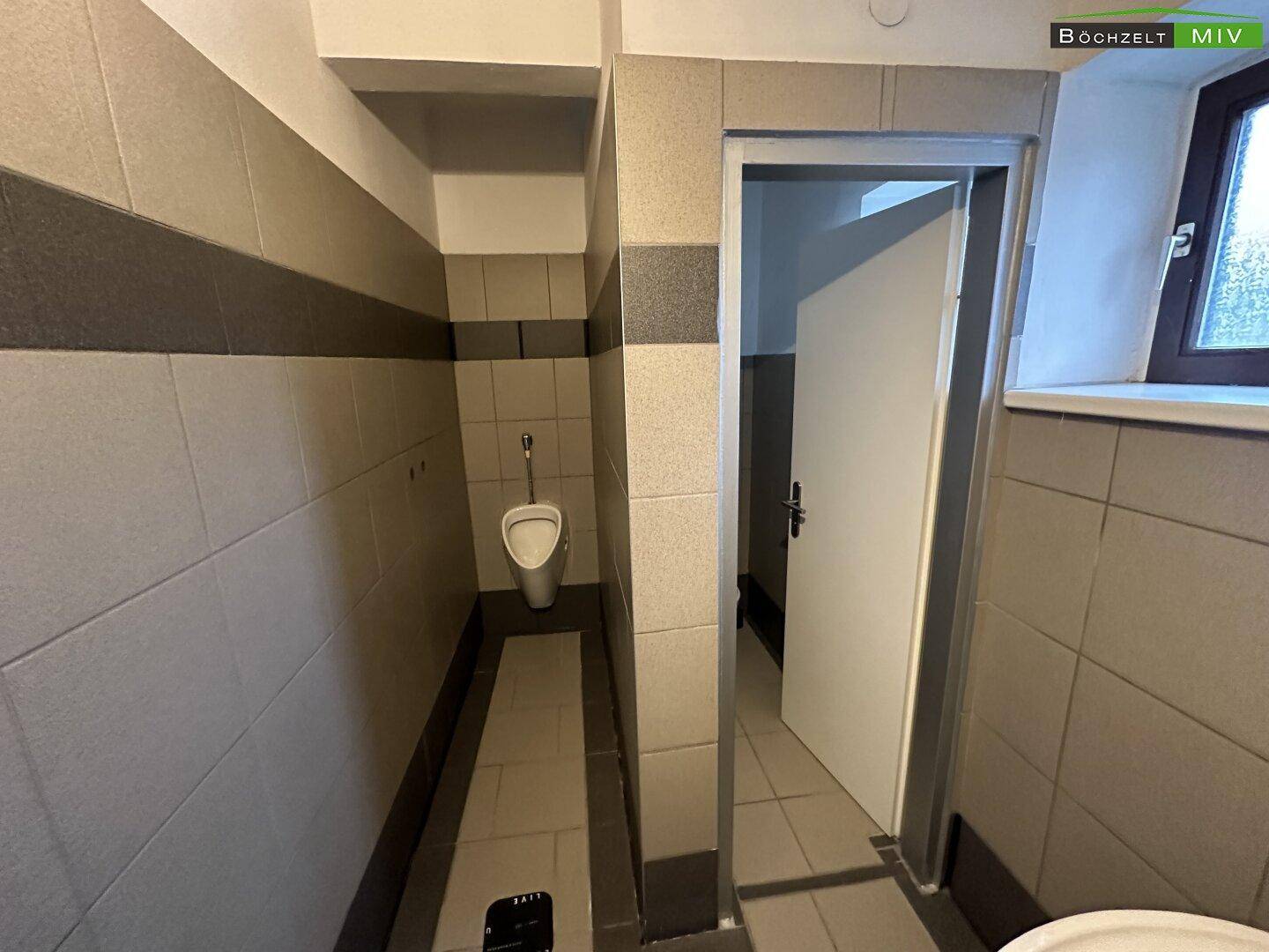 Toilettenraum mit Urinal, gefliesten Wänden und einem Fenster für natürliche Belüftung und Helligkeit.