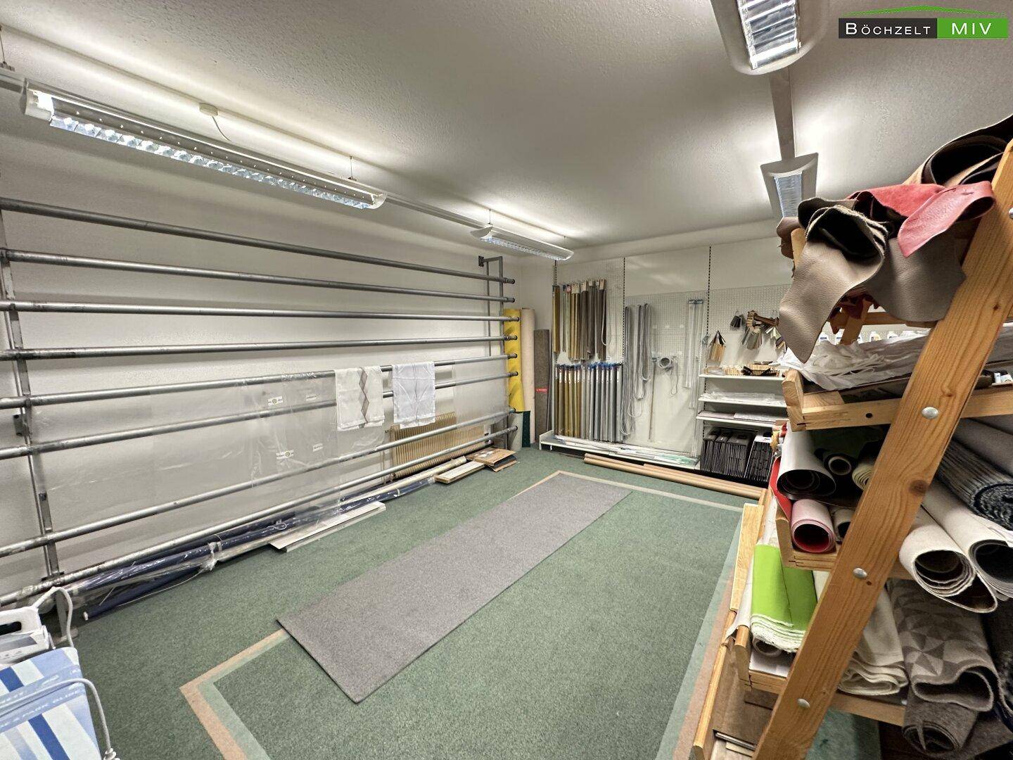 Lagerraum oder Werkstatt mit Regalen, Materialrollen und Teppichboden in einem gewerblichen Bereich.