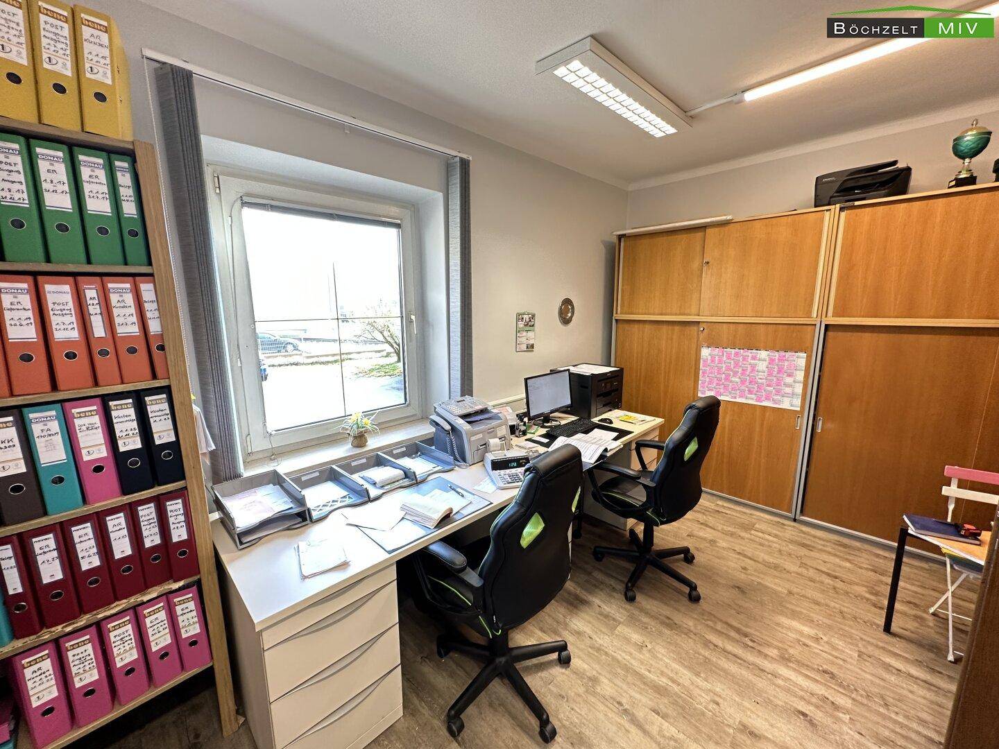 Helles Büro mit großem Fenster, Schreibtisch, Bürostühlen und Aktenschränken.