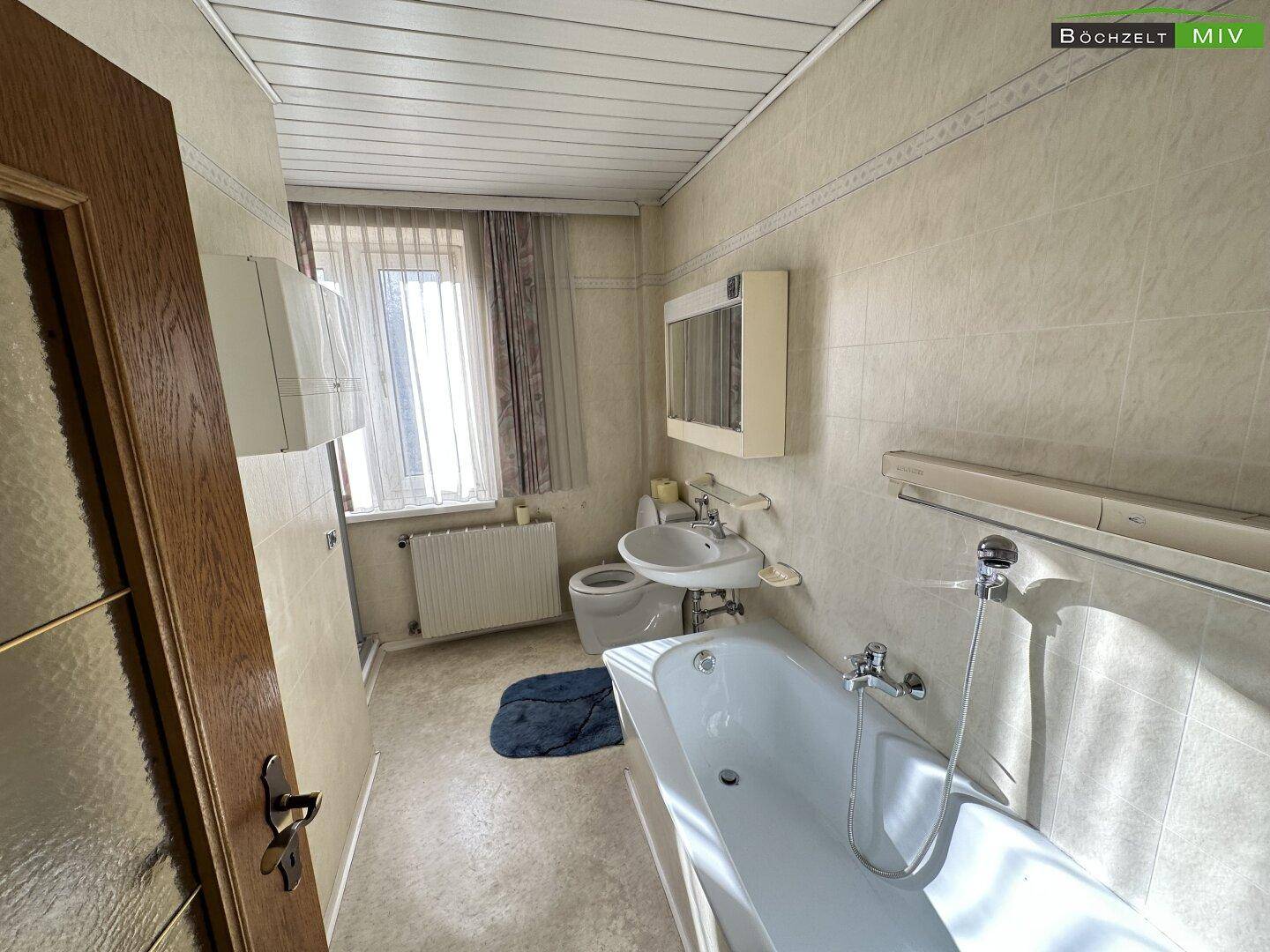 Badezimmer mit Badewanne, Waschbecken, WC und Fenster, in einem älteren Stil gehalten.