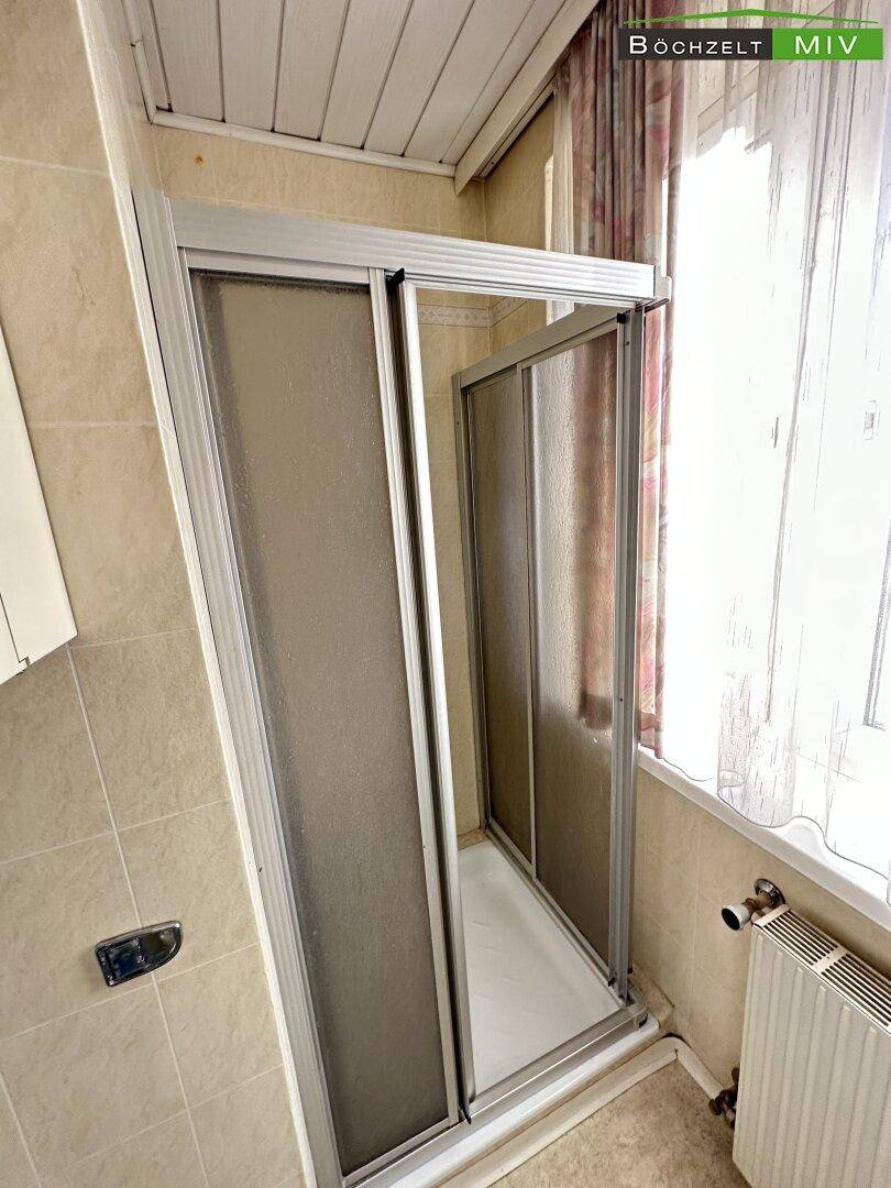 Duschkabine mit Schiebetüren in einem gefliesten Badezimmer mit Fenster.