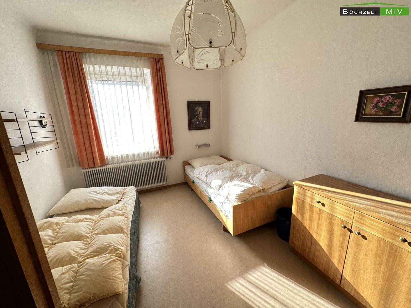 Schlafzimmer mit zwei Einzelbetten, Holzmöbeln und einem Fenster, das viel Licht hereinlässt.