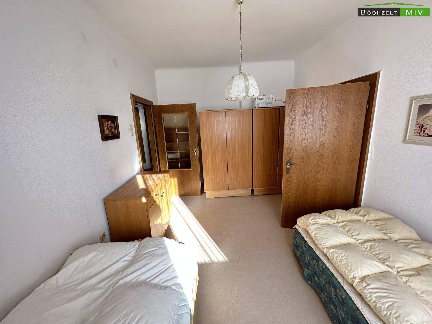 Schlafzimmer mit zwei Betten und Holzschränken, das viel Tageslicht empfängt.