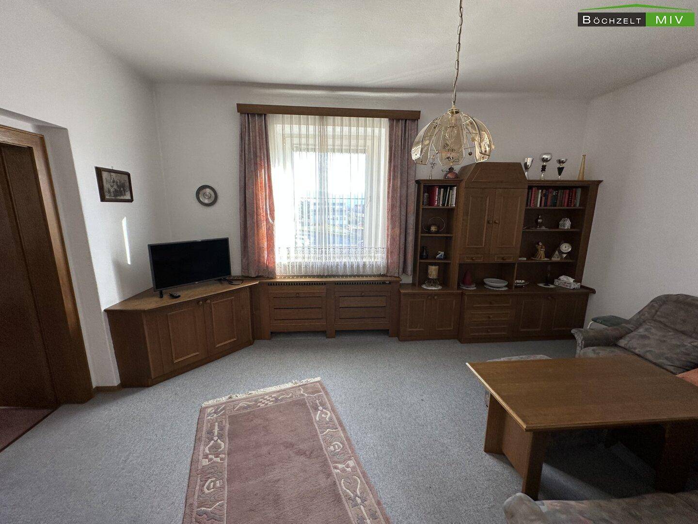 Gemütliches Wohnzimmer mit Sofa, Teppich und Holzeinrichtung, das viel Tageslicht erhält.