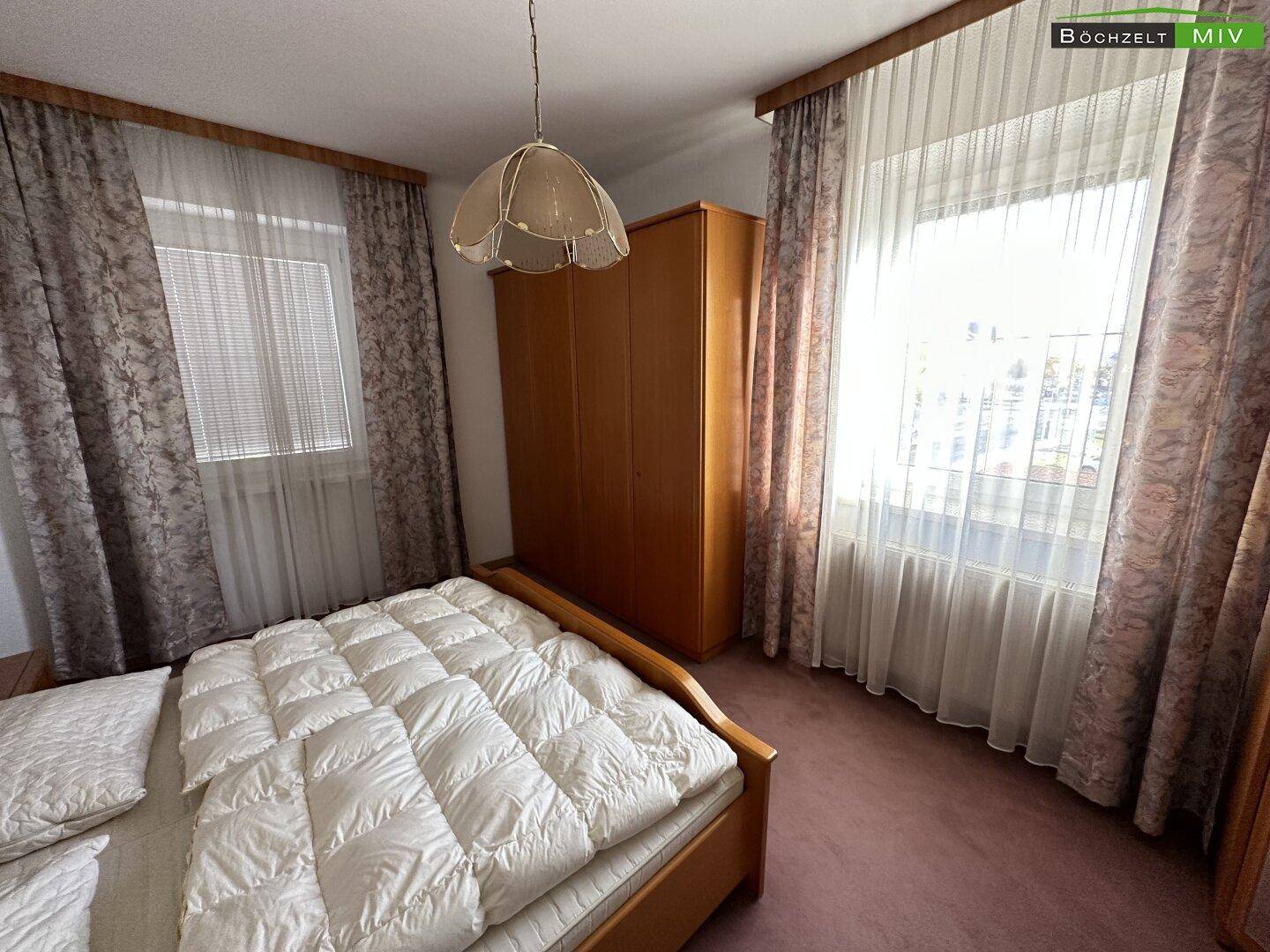 Schlafzimmer mit Doppelbett, großem Kleiderschrank und zwei Fenstern für viel Licht.