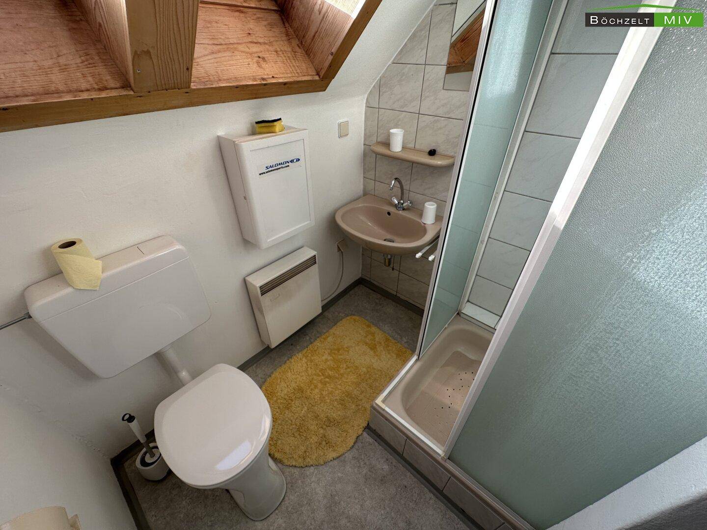 Kleines Badezimmer in einer Dachgeschosswohnung mit Dusche, WC und Waschbecken unter der Dachschräge.