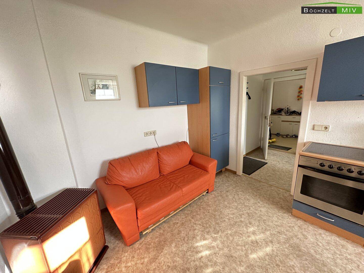 Wohnbereich in einer Dachgeschosswohnung mit Sofa, Küchenzeile und schrägen Wänden.