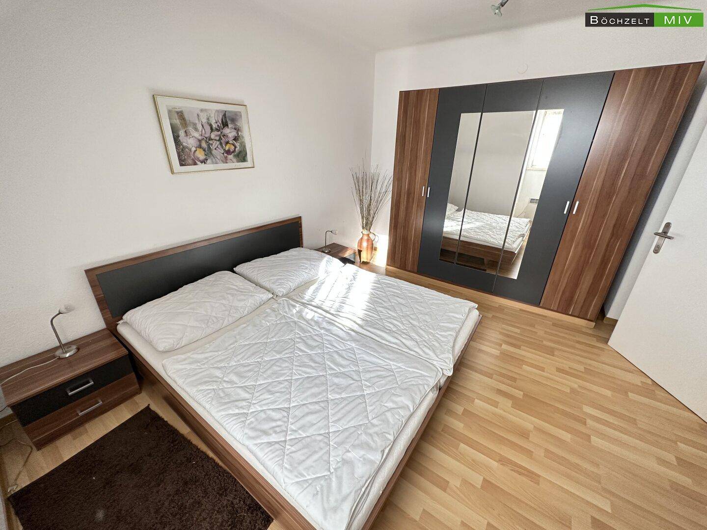 Modernes Schlafzimmer mit Doppelbett, großem Spiegelschrank und Laminatboden.