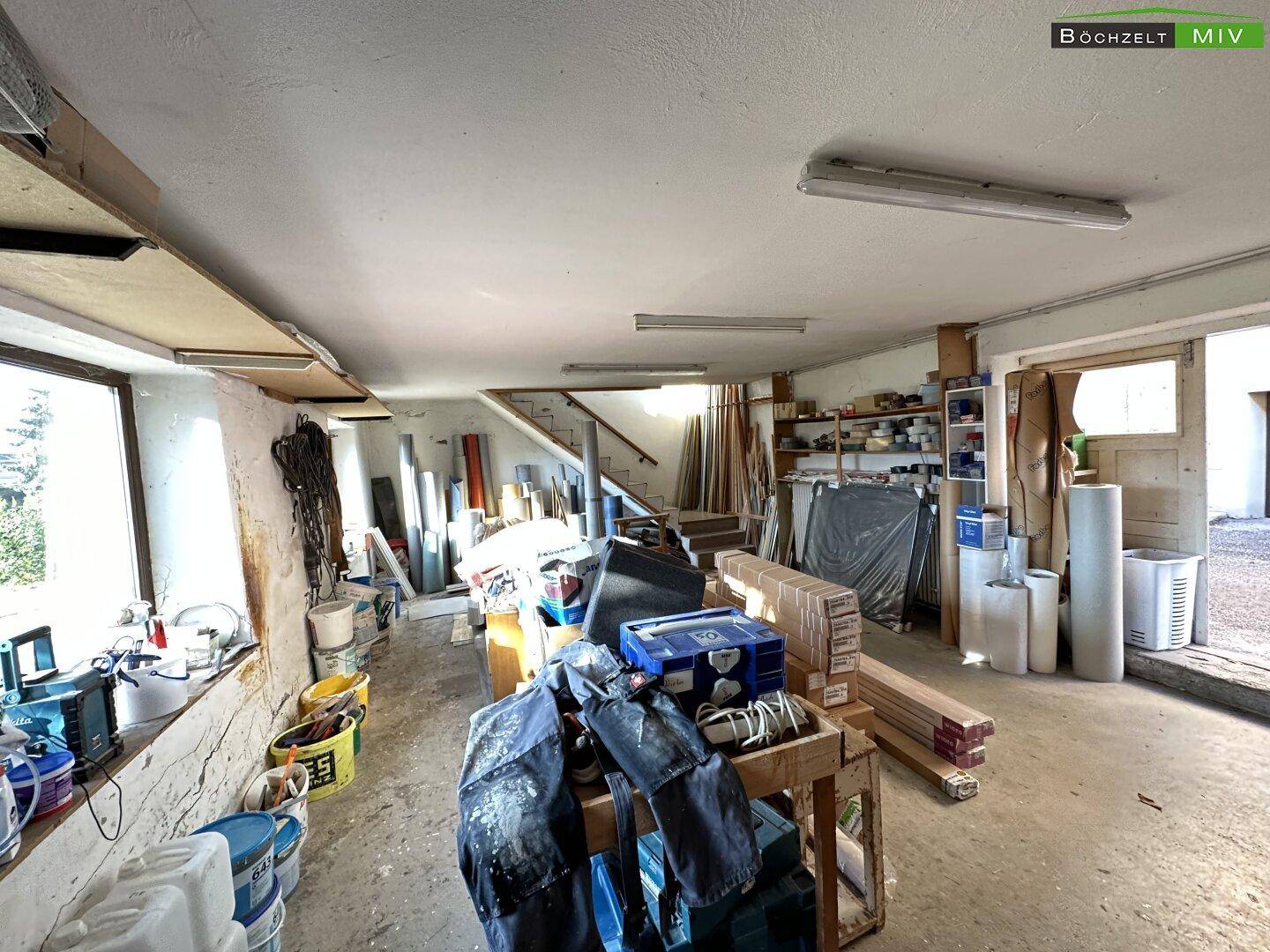 Geräumige Werkstatt oder Lagerhalle mit großen Fenstern und verschiedenen Arbeitsmaterialien.