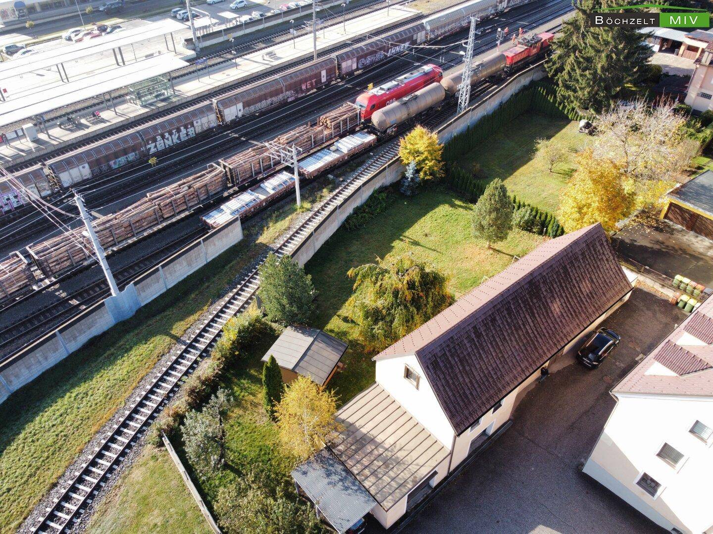Draufsicht auf die Bahngleise neben dem Grundstück mit Herbstbäumen und Gebäuden.