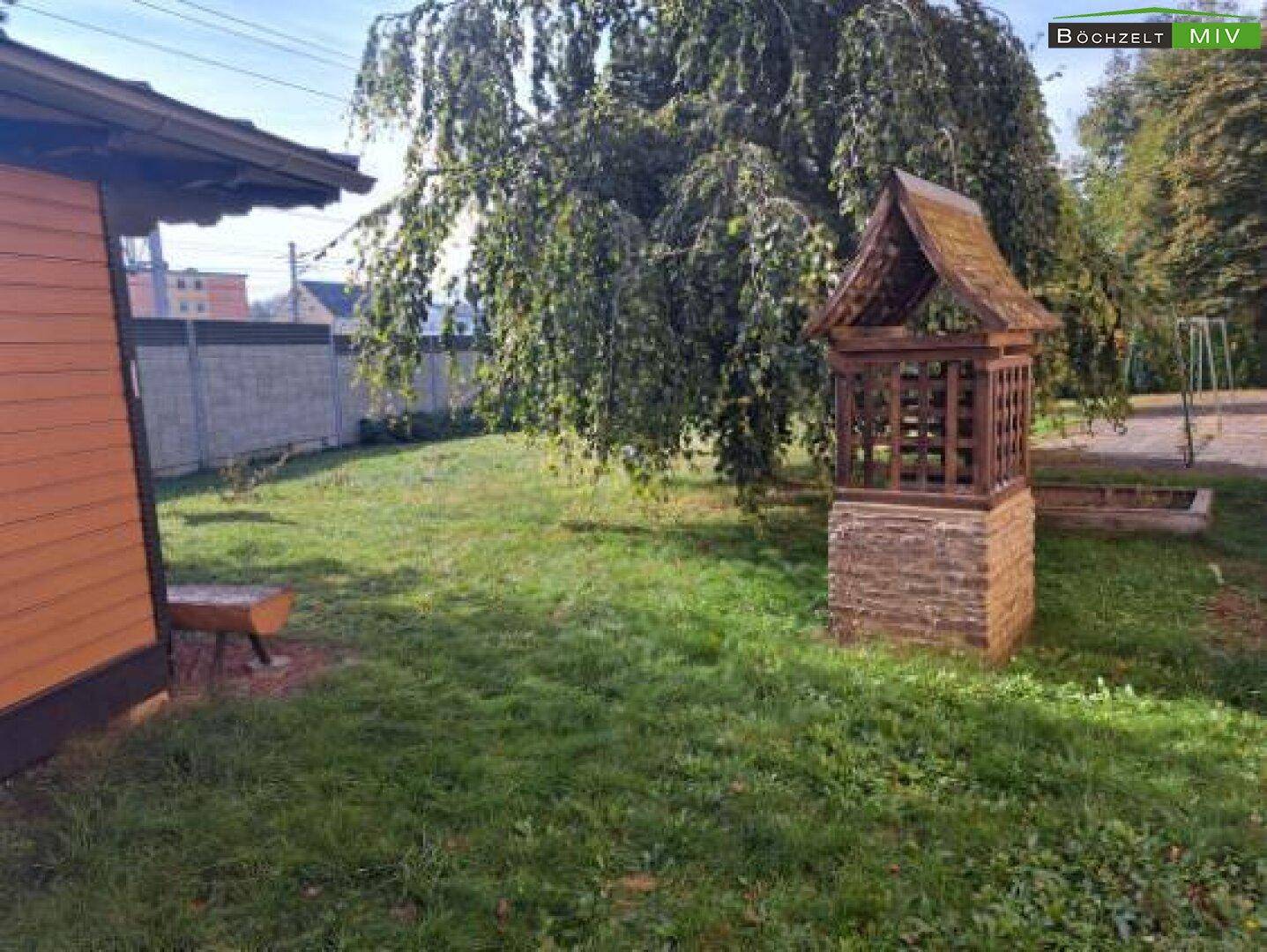Gepflegter Gartenbereich mit Rasenfläche, einem Zierbrunnen und altem Baumbestand.