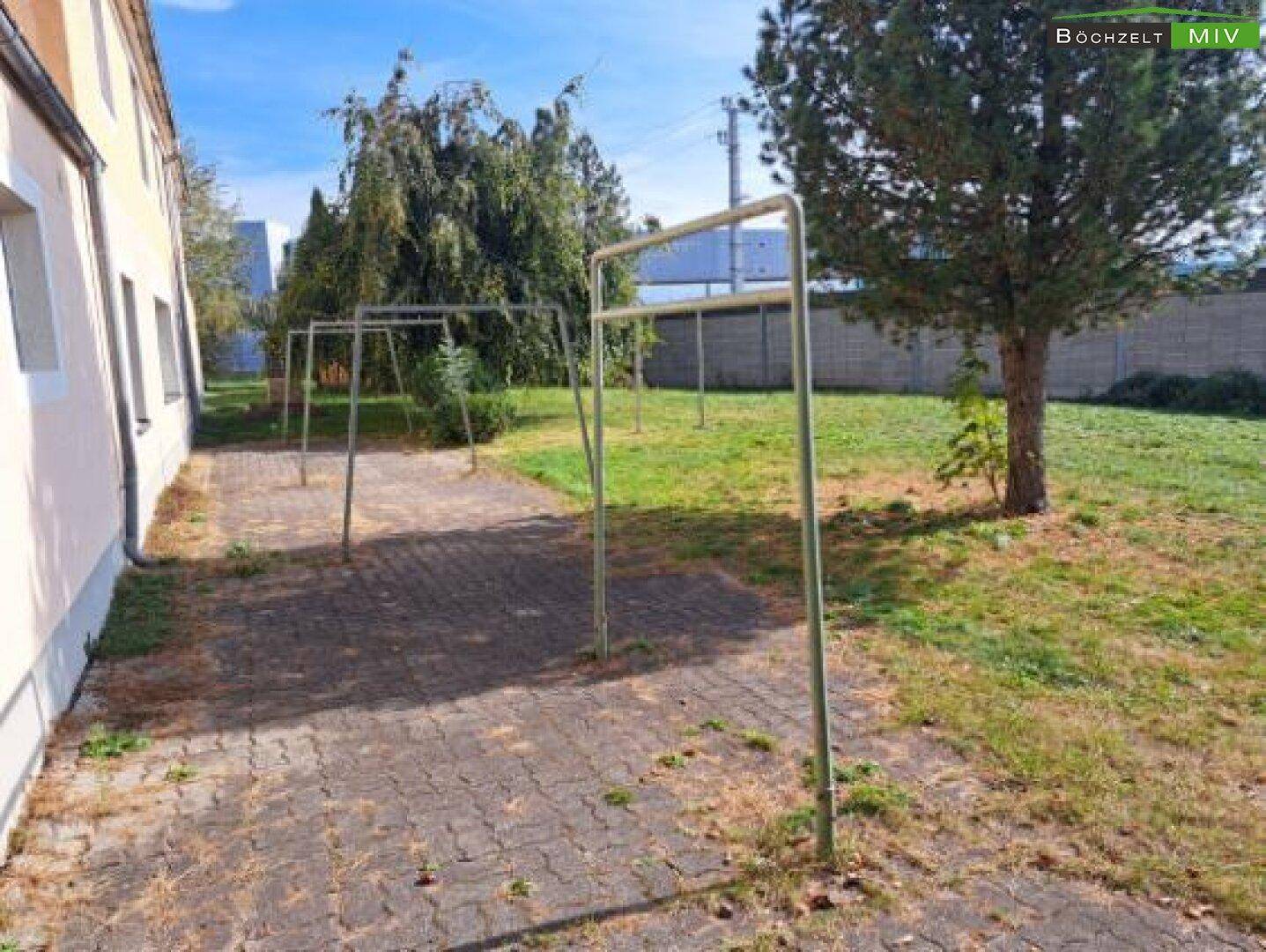 Gartenbereich mit gepflastertem Weg und einem Schaukelgestell, ideal für Kinder.