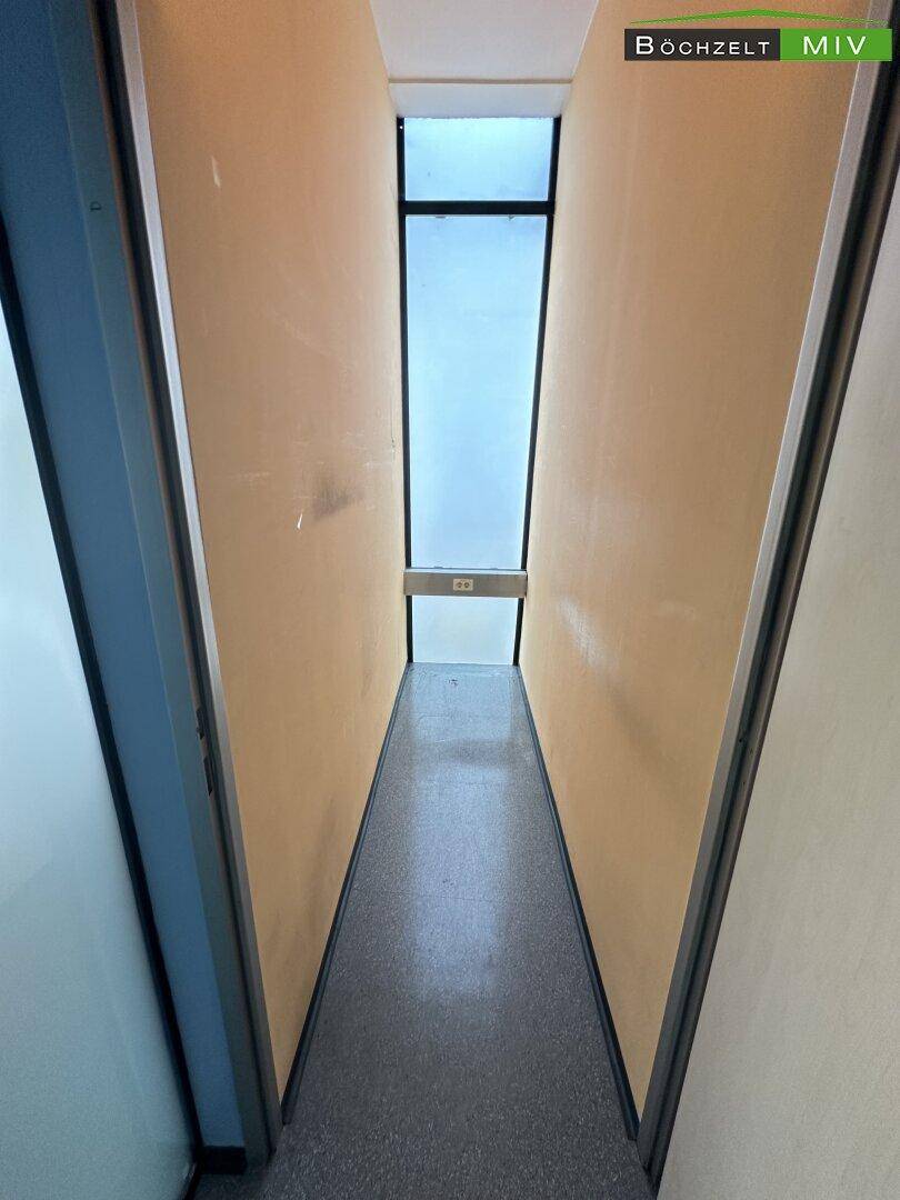 Schmaler Flur mit Oberlicht, der zu einem weiteren Bereich führt und gut beleuchtet ist.