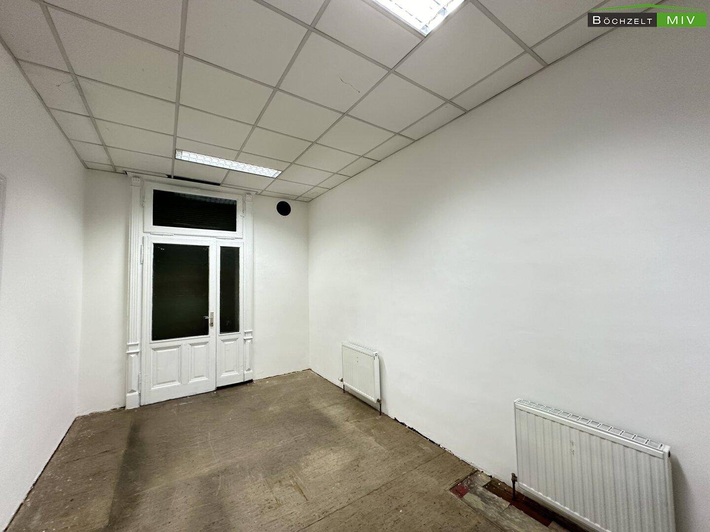 Leerer Raum mit doppelter Eingangstür, abgehängter Decke und zwei Heizkörpern, ideal für Gewerbe.