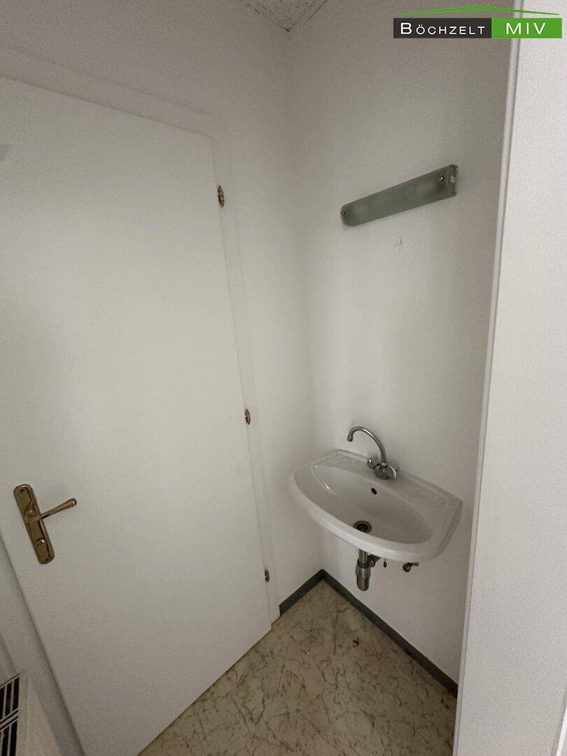 Kleiner Waschraum mit einem einfachen Waschbecken und einer Tür, funktional und kompakt gestaltet.
