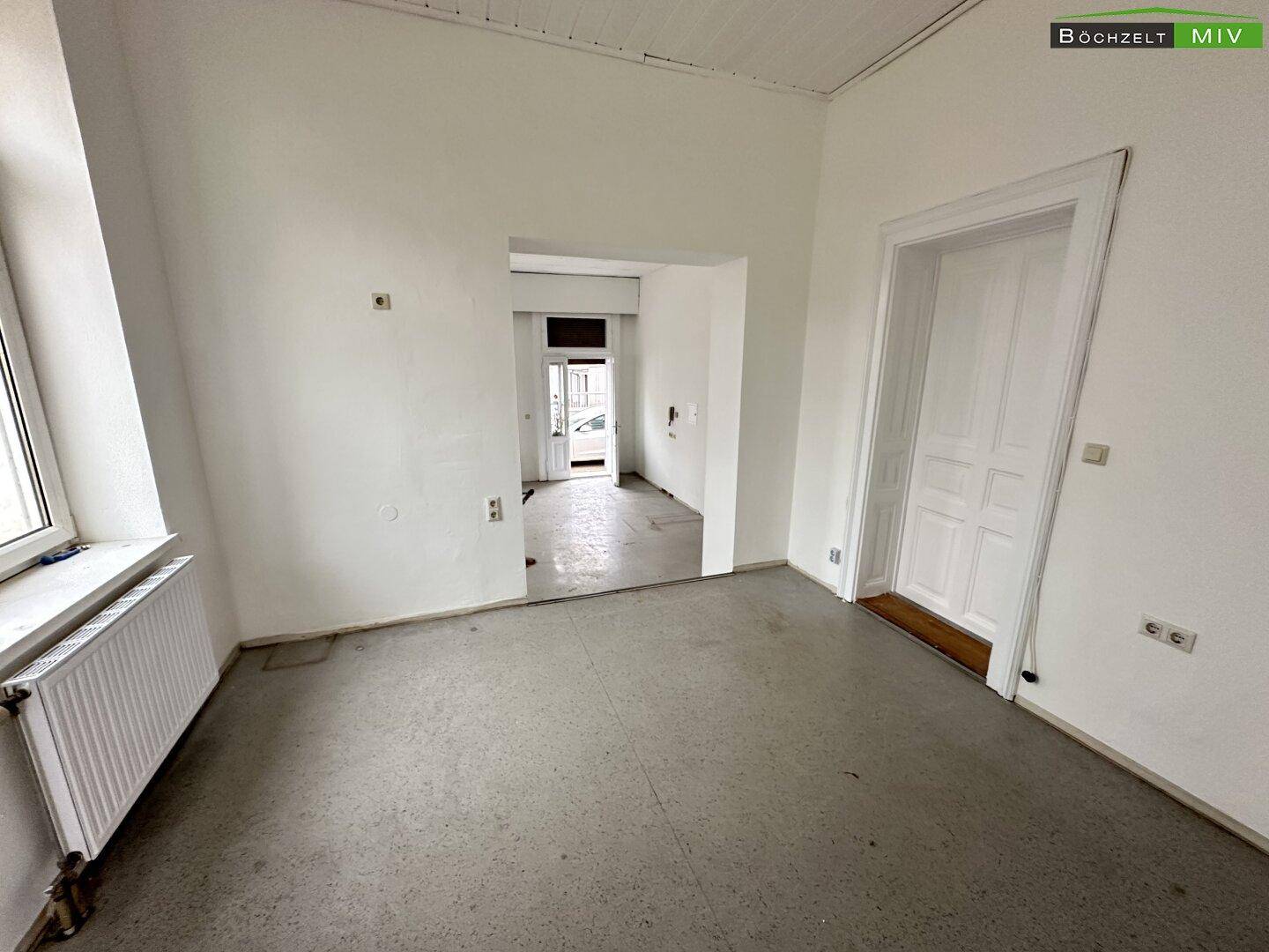 Geräumiger Gewerberaum mit hohen Decken, weißen Wänden und einem Durchgang zu einem weiteren Bereich.