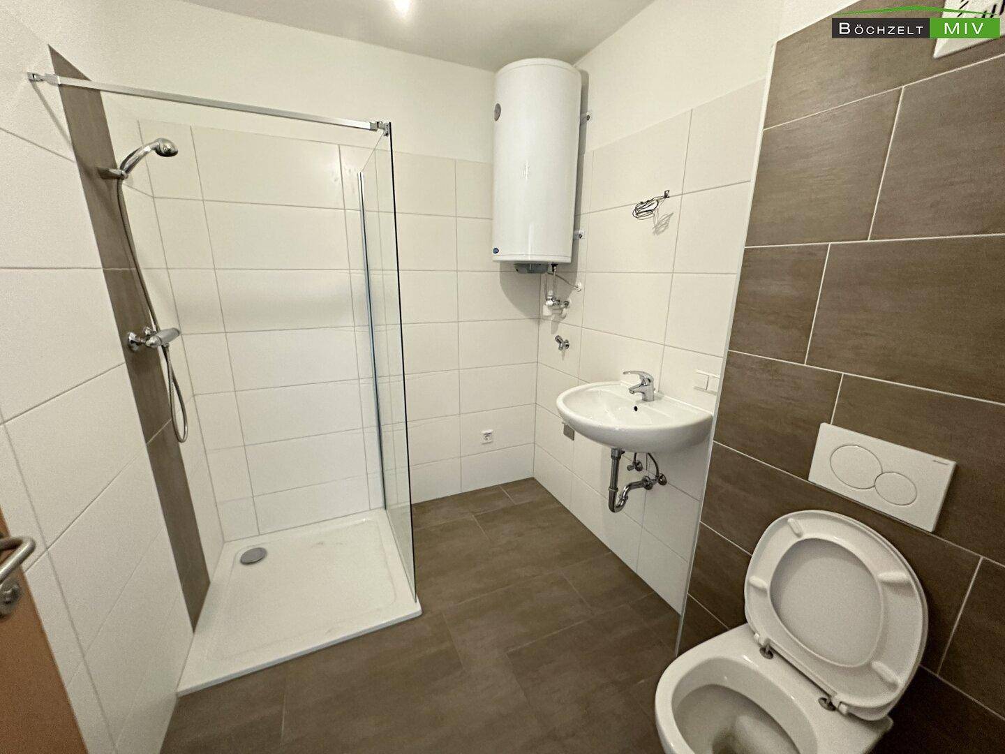 Funktionales Badezimmer mit Duschbereich, WC und Waschbecken, gefliest in neutralen Farben für eine saubere Optik.